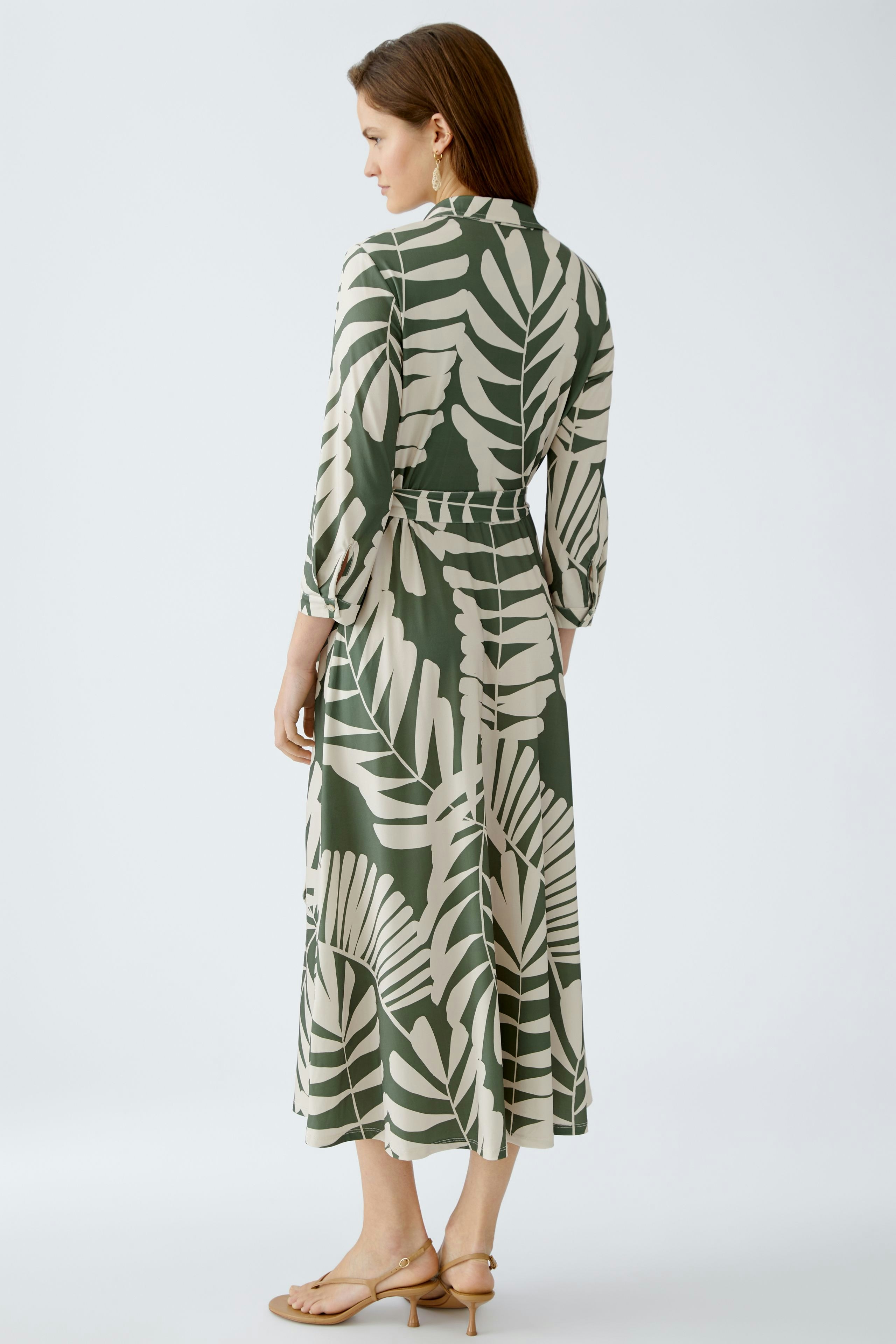 Hemdblusenkleid: Frau trägt ein elegantes, gemustertes Kleid mit langen Ärmeln und Taillengürtel.