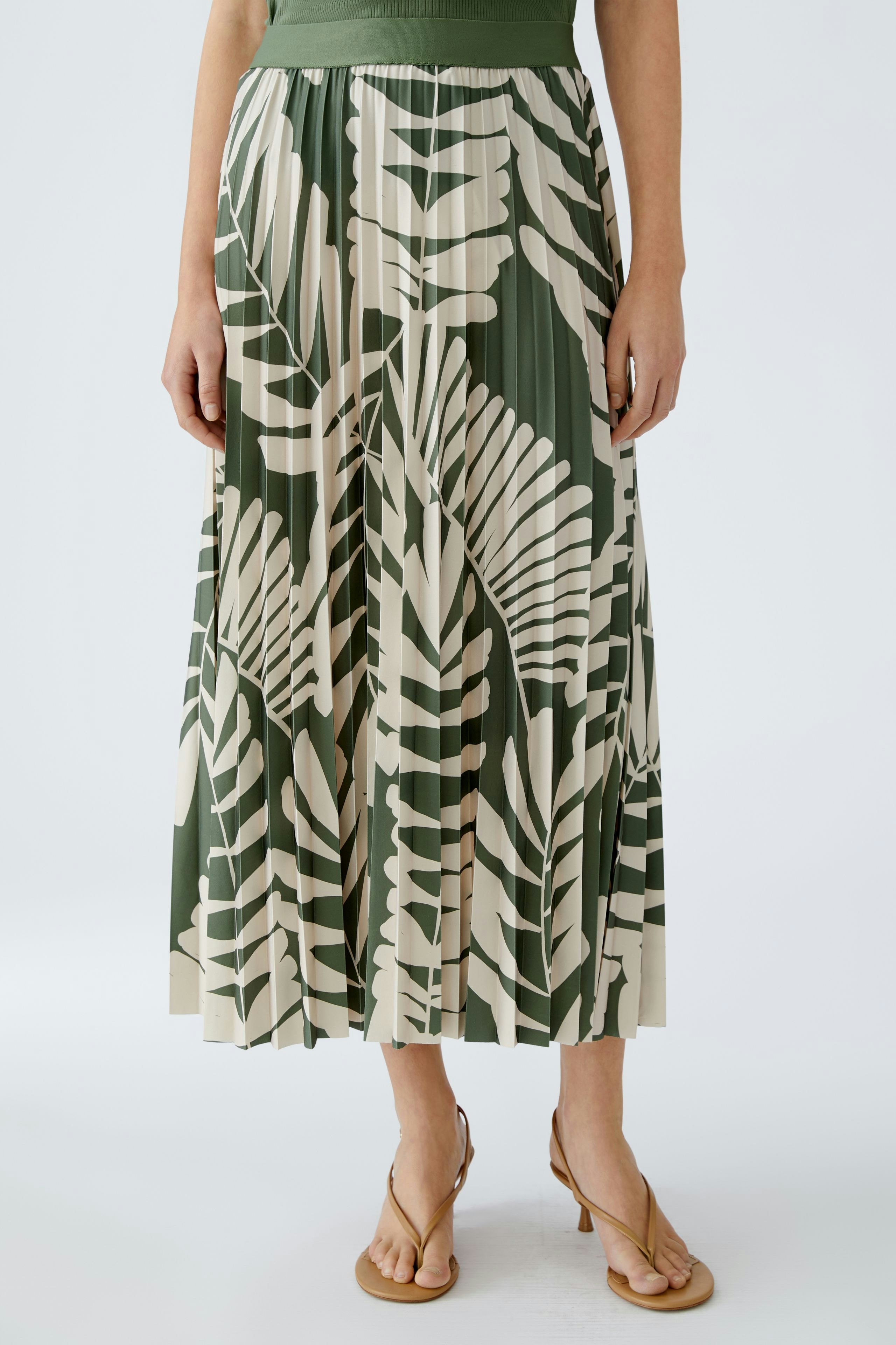 Eleganter Plisseerock: Frau trägt einen langen Rock mit grün-weißen Blattmustern.