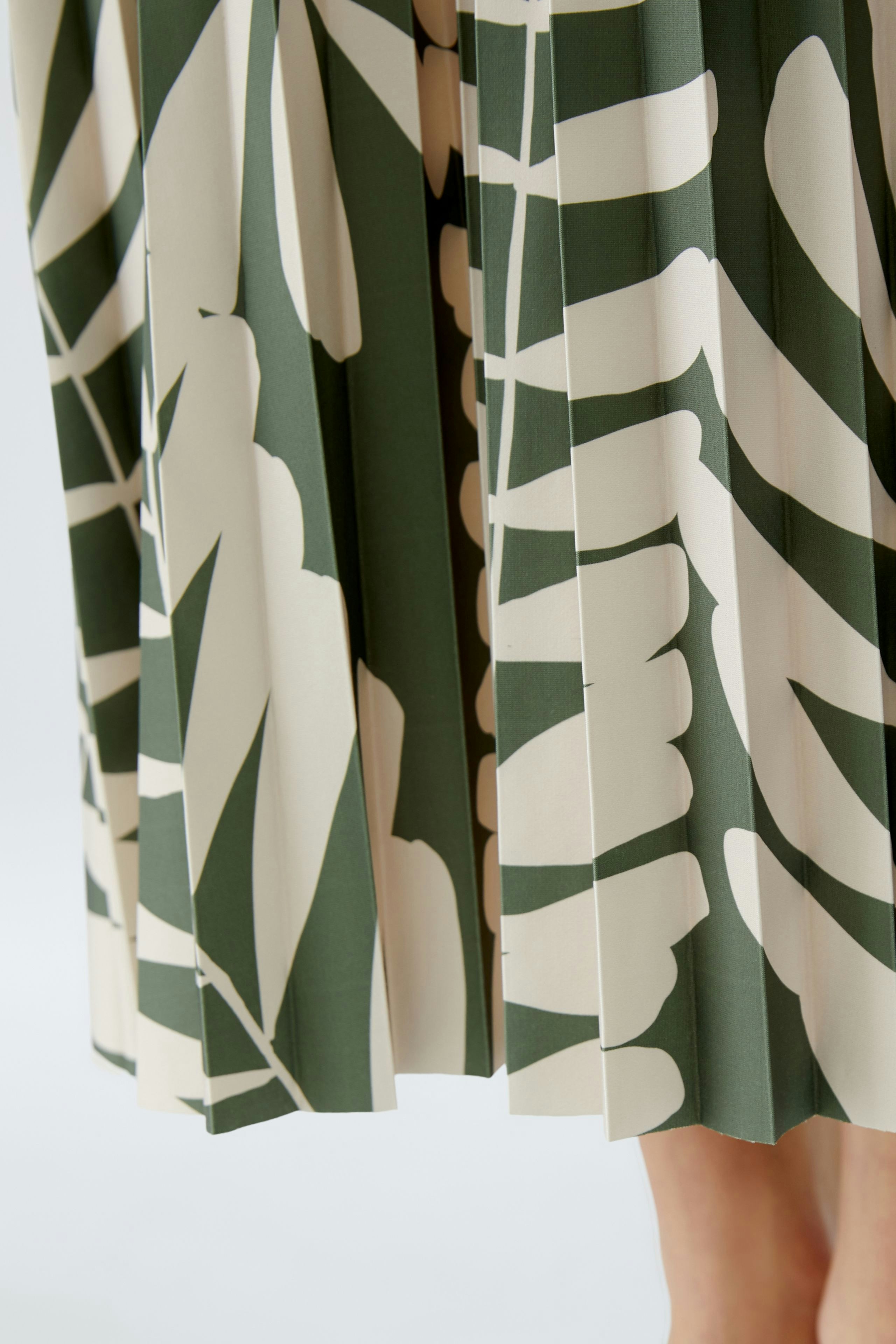 Eleganter Plisseerock: Detailansicht eines grünen Rocks mit stilvollem Blattmuster.