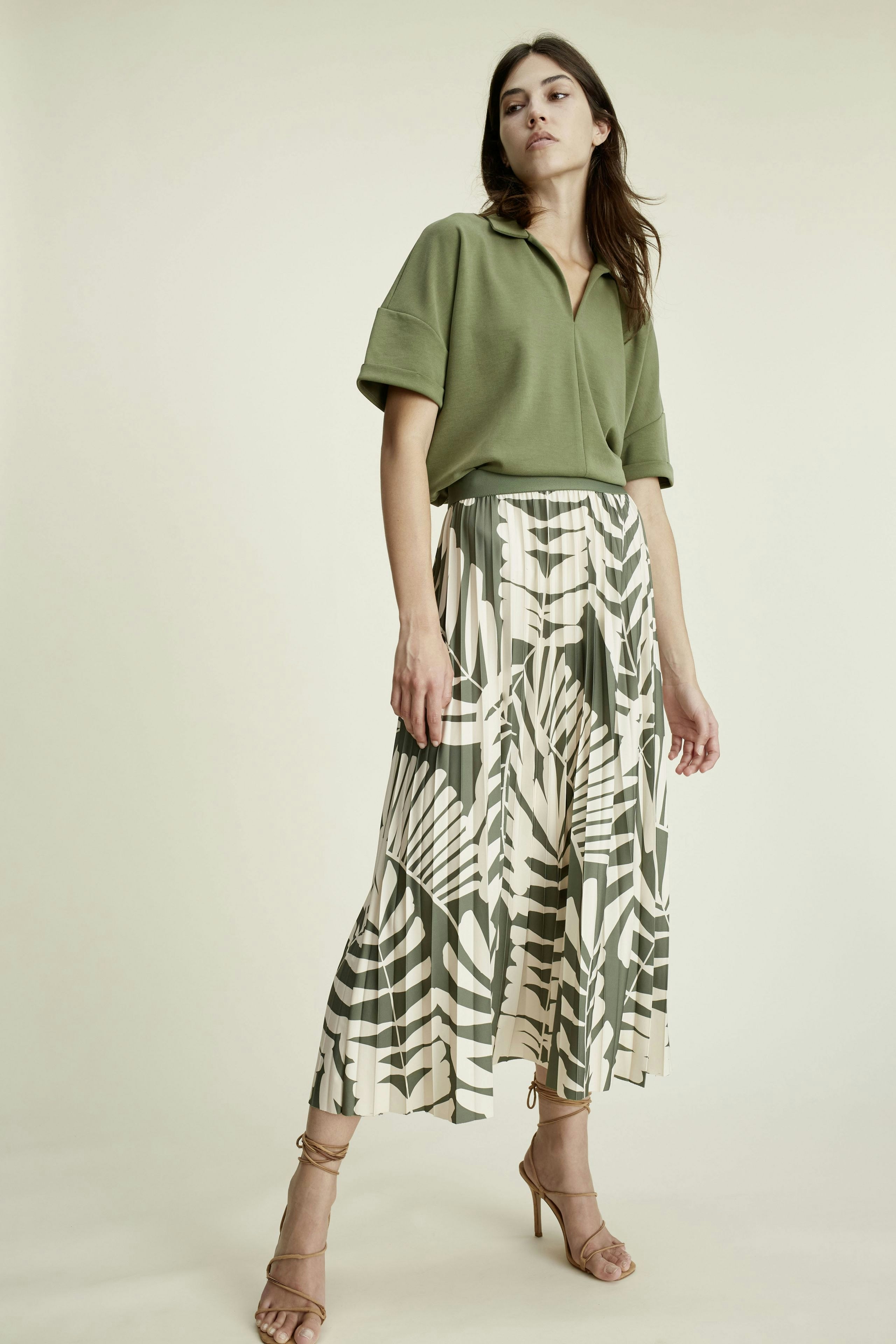 Eleganter Plisseerock: Frau trägt einen modischen, gemusterten Plisseerock in sanften Grüntönen.