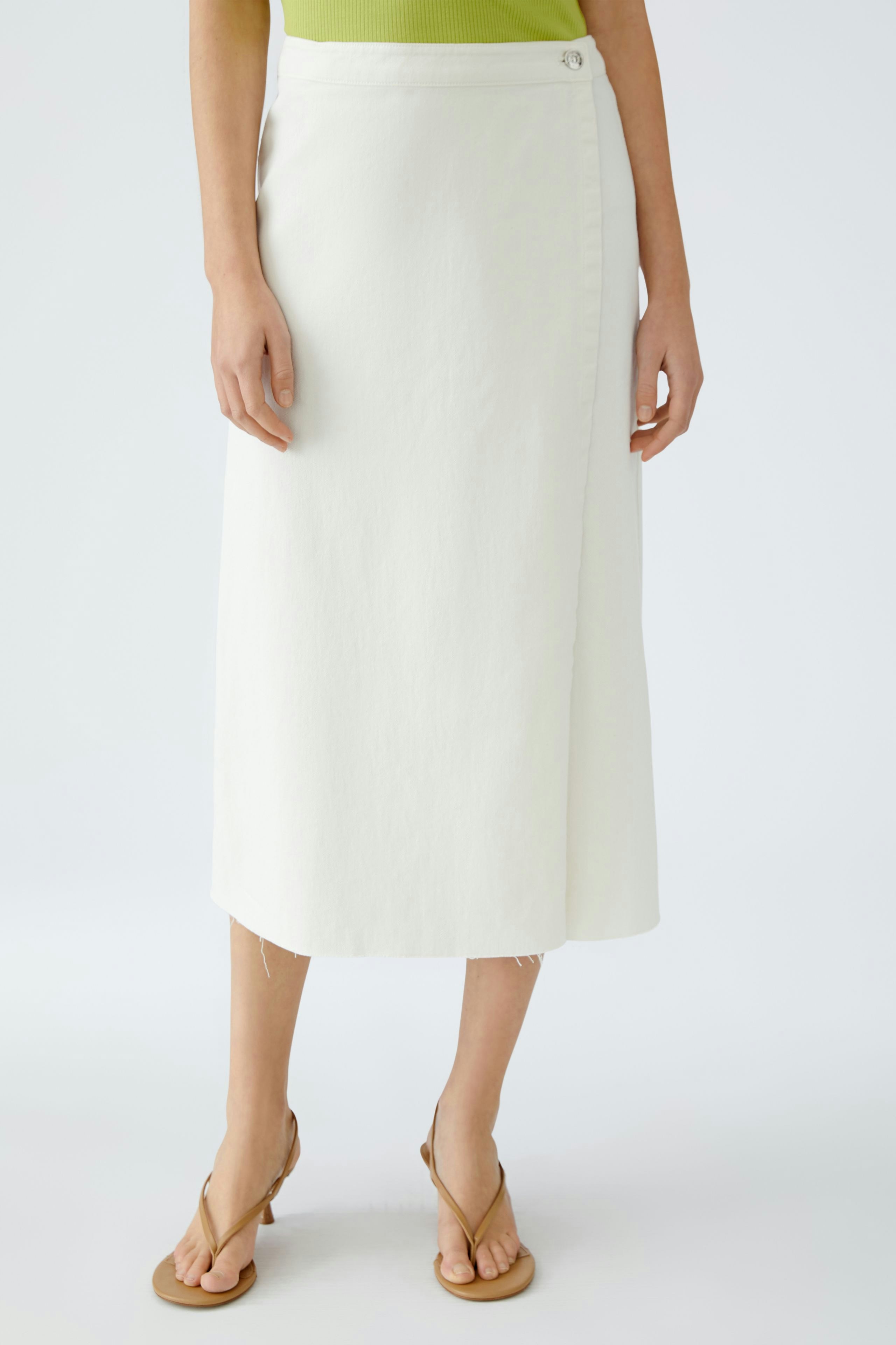 Eleganter Wickelrock: Frau in einem weißen Wickelrock mit Knopfdetails und lässigen Sandalen.