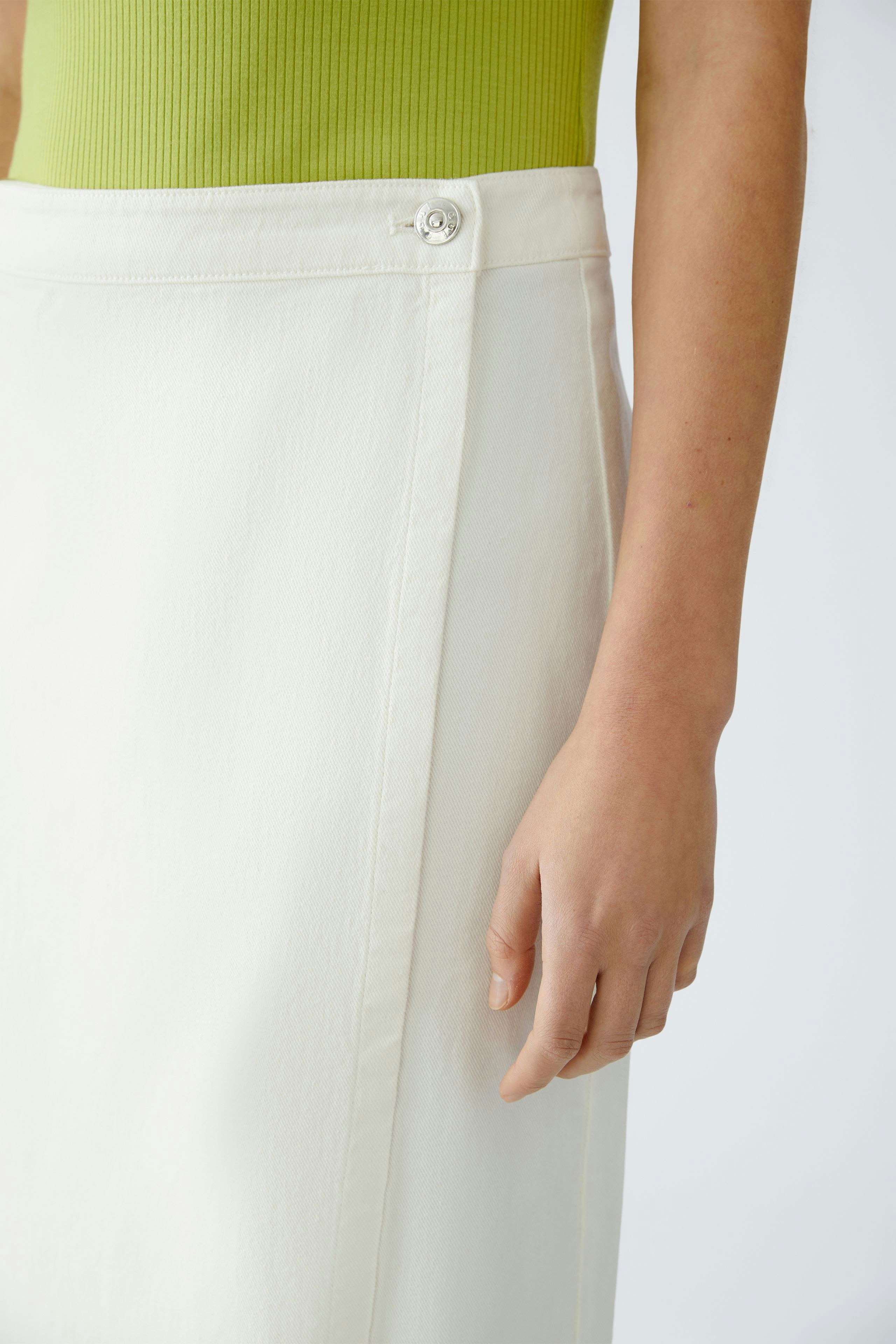Eleganter Wickelrock: Frau trägt einen weißen Wickelrock mit Knopfdetails und kombiniert ihn mit einem grünen Oberteil.