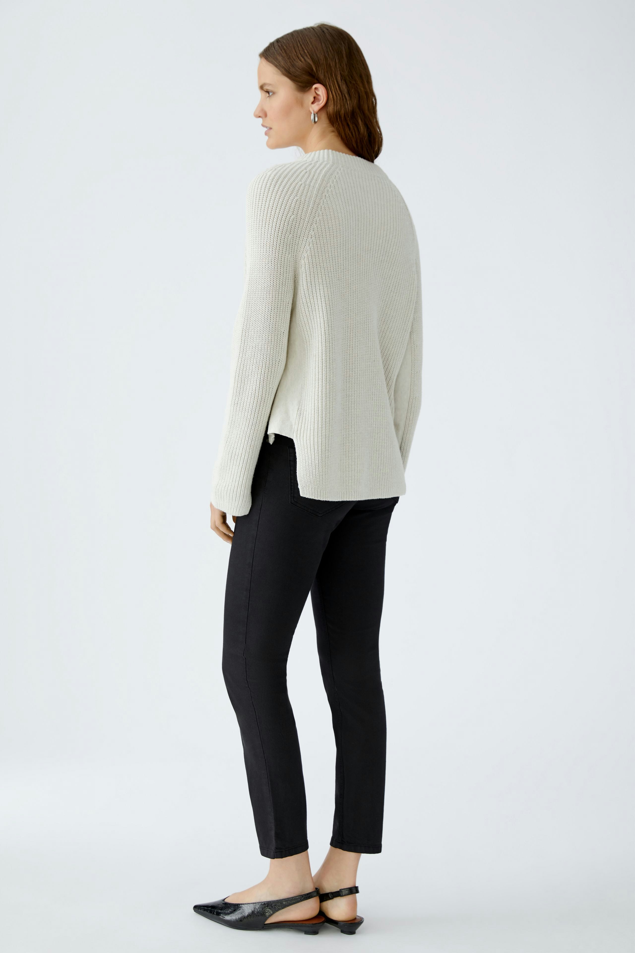 Damen-Pullover: Frau in hellem Strickpullover mit lässigem Schnitt und schwarzer Hose von hinten.