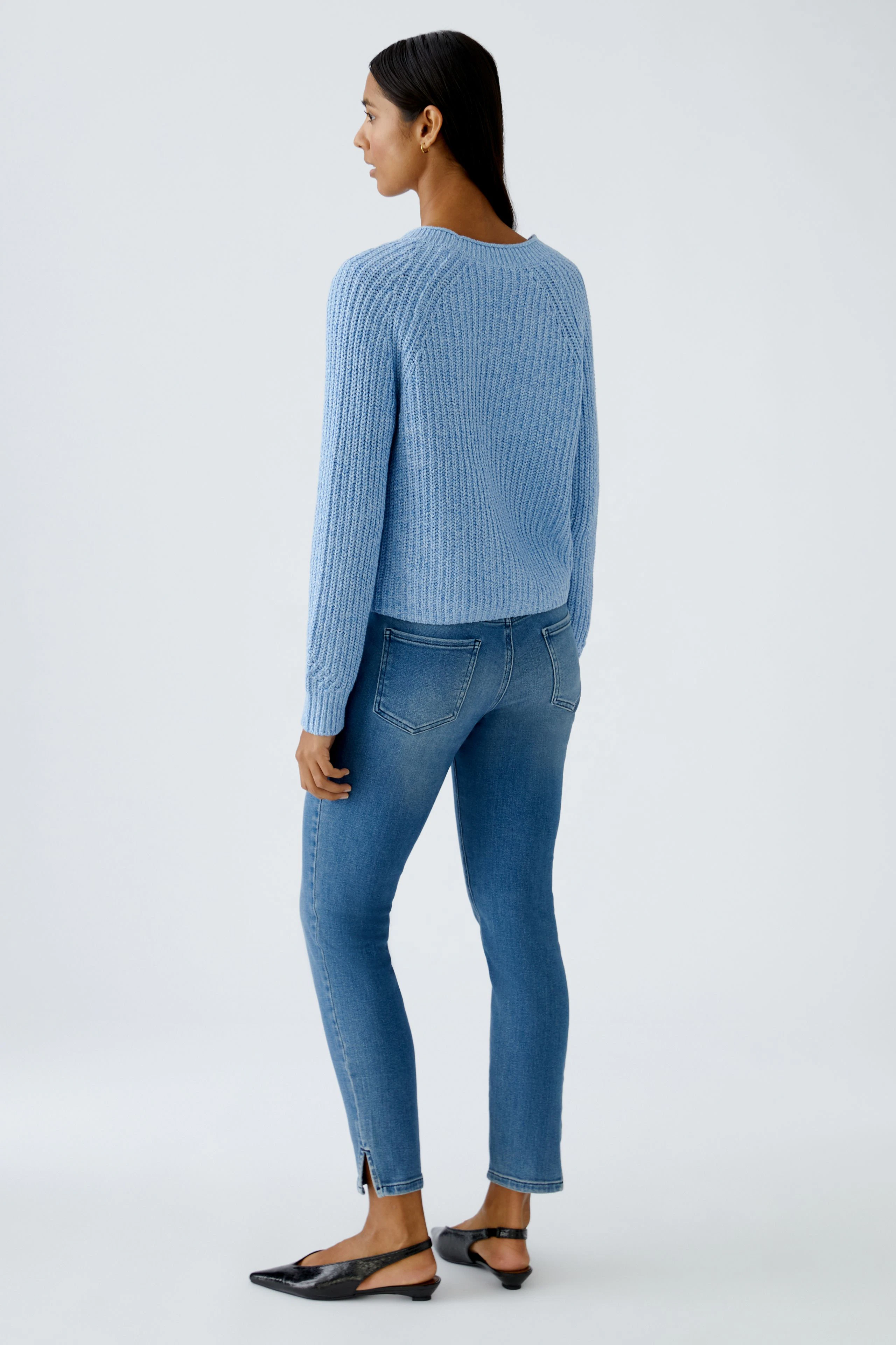 Damen-Strickjacke: Frau in blauer Strickjacke mit lässigem Schnitt und weißen Jeans von hinten.