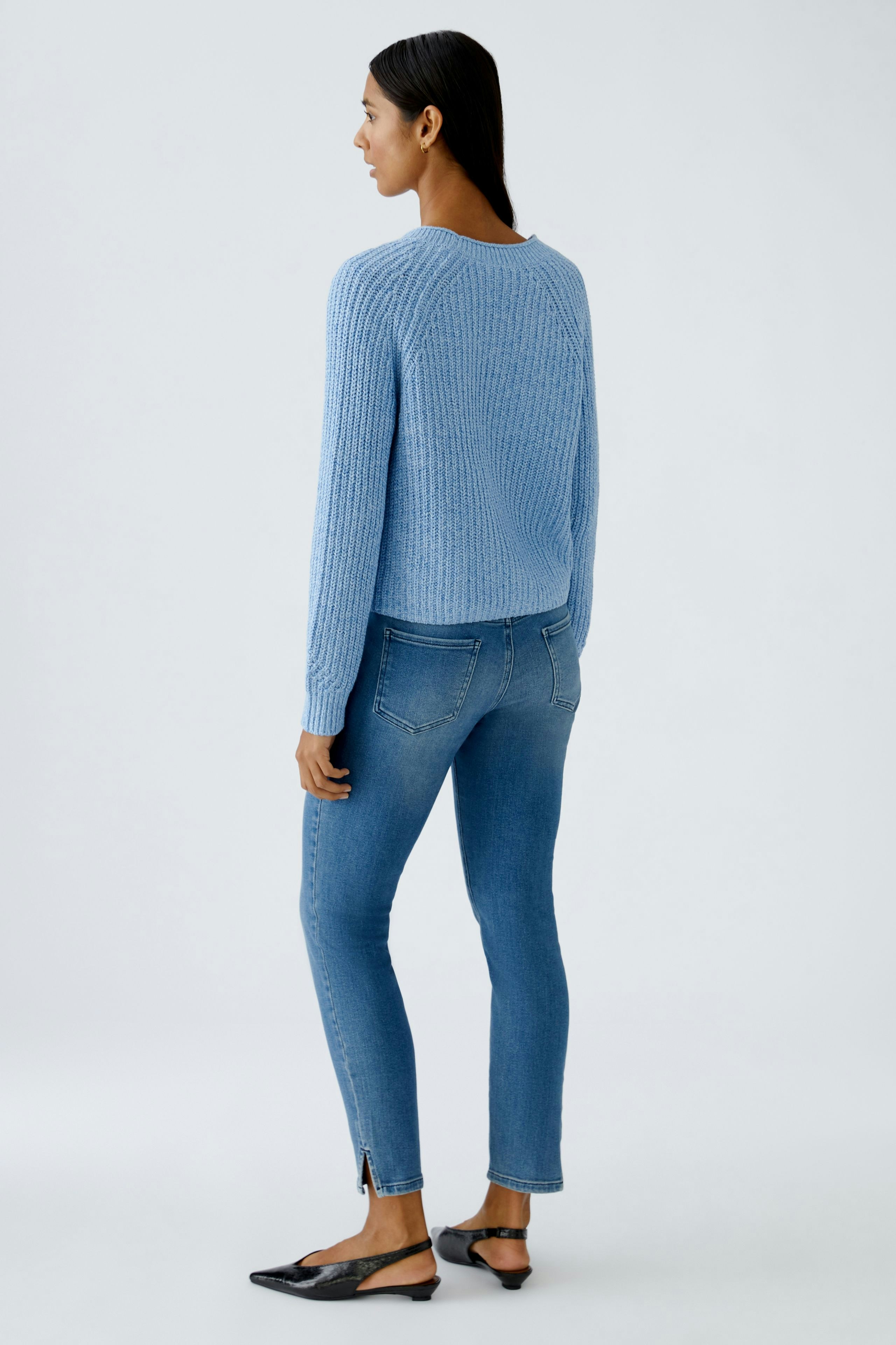 Damen-Strickjacke: Frau in blauer Strickjacke mit lässigem Schnitt und weißen Jeans von hinten.