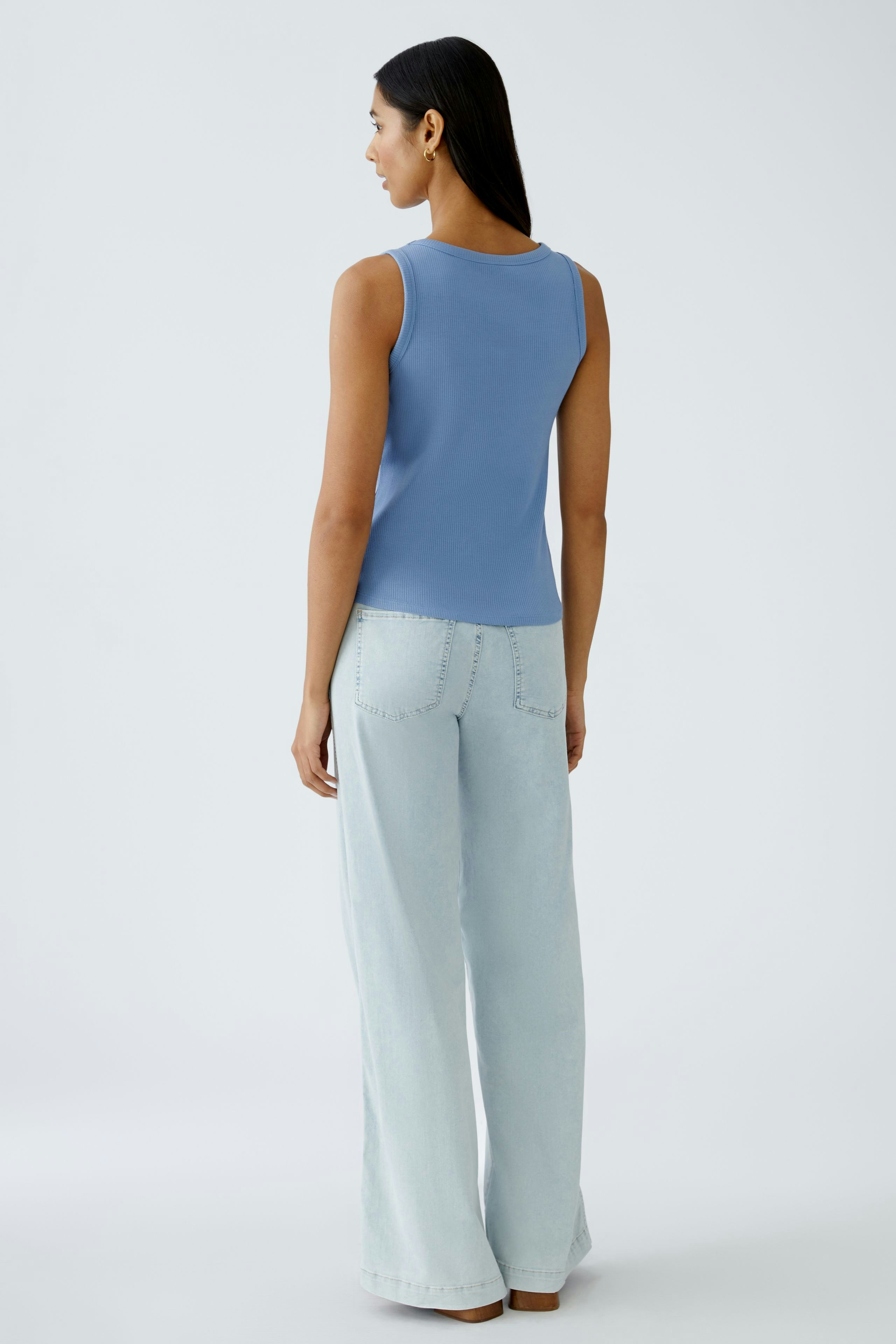 Stylish women's top: A woman in a light blue sleeveless top paired with light jeans.