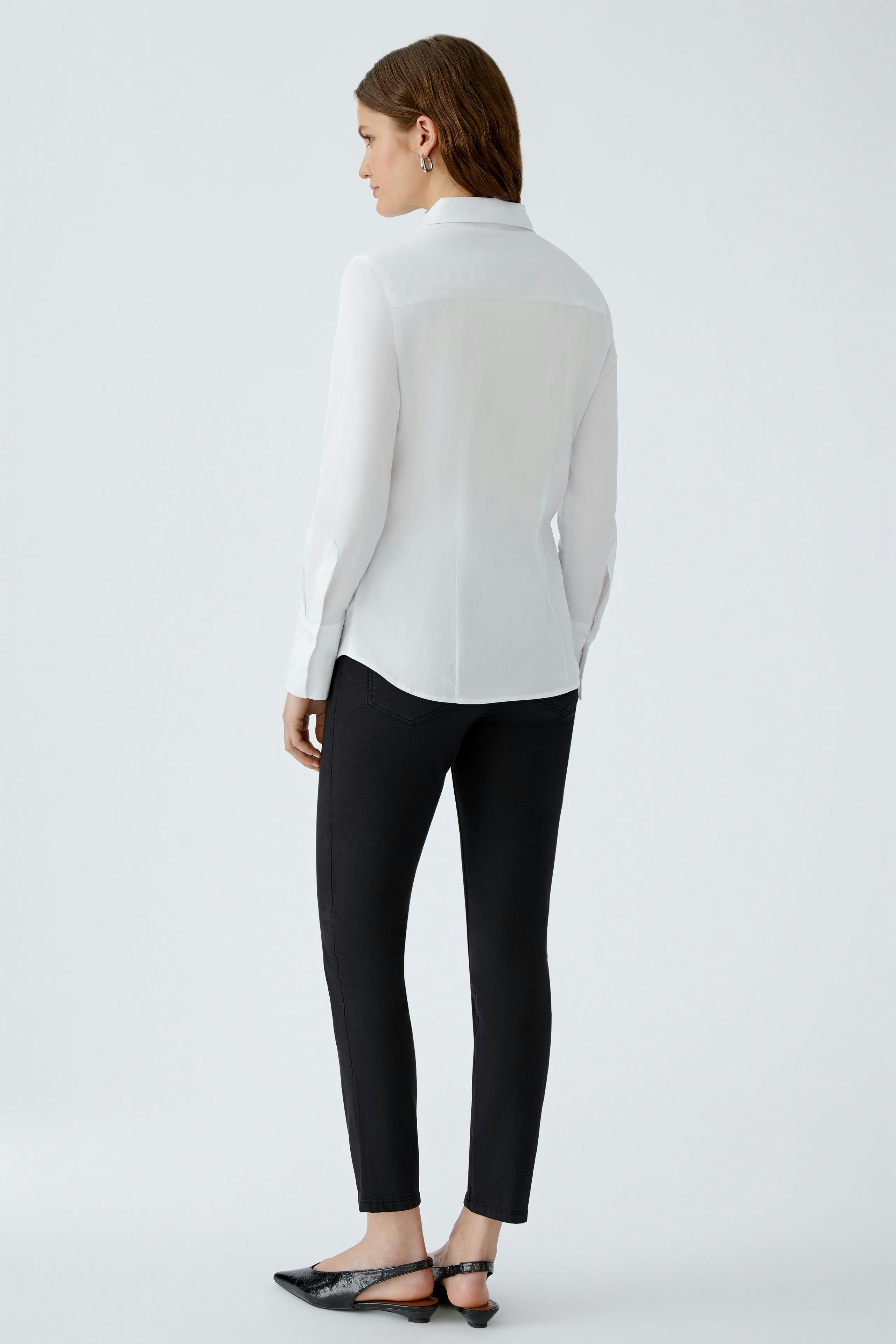 Elegante Damen-Bluse: Frau in weißer Bluse mit langen Ärmeln und klassischem Schnitt von hinten.