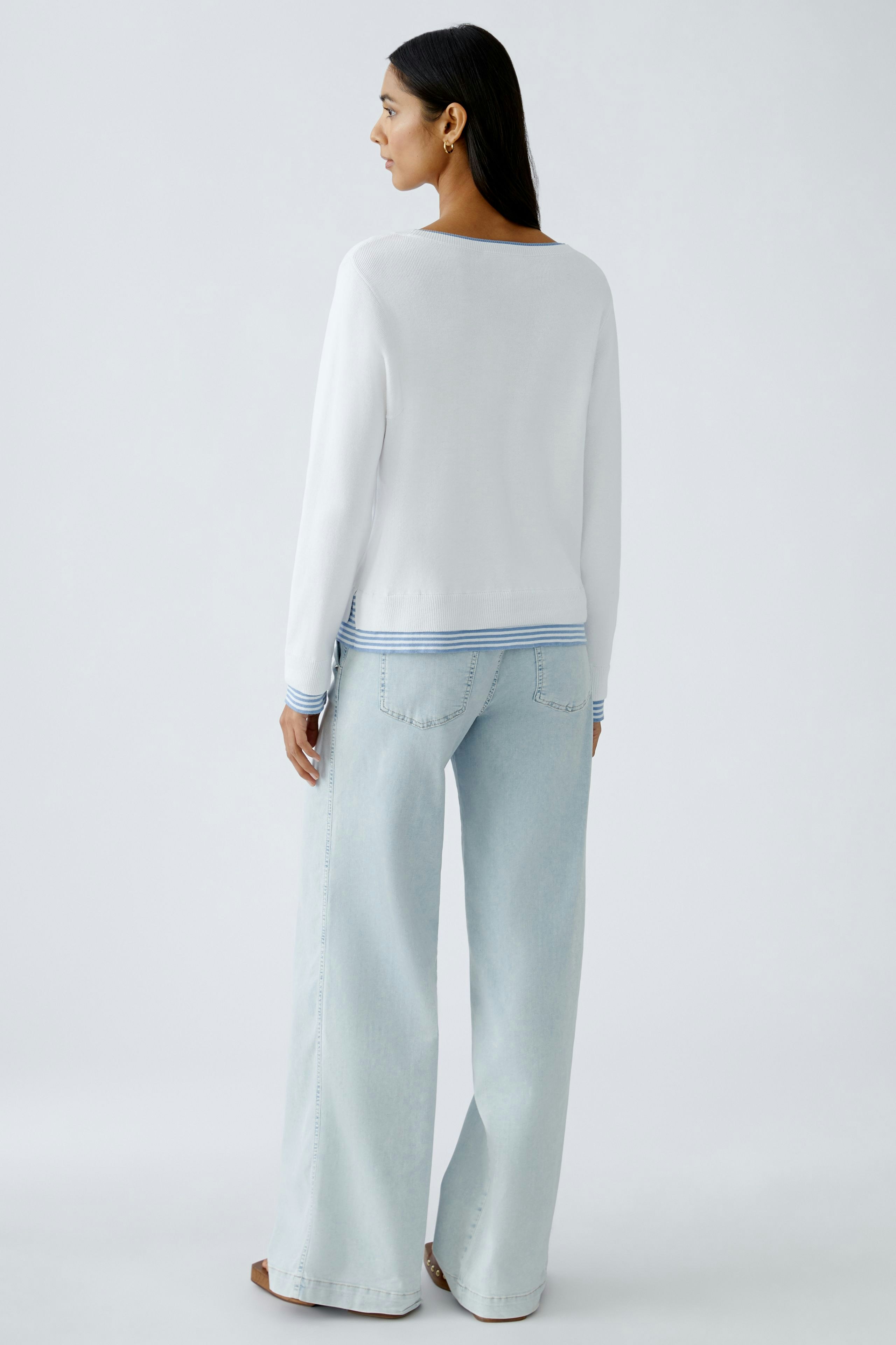 Stylish women's pullover: A woman in a white pullover with a blue striped hem, paired with light jeans.