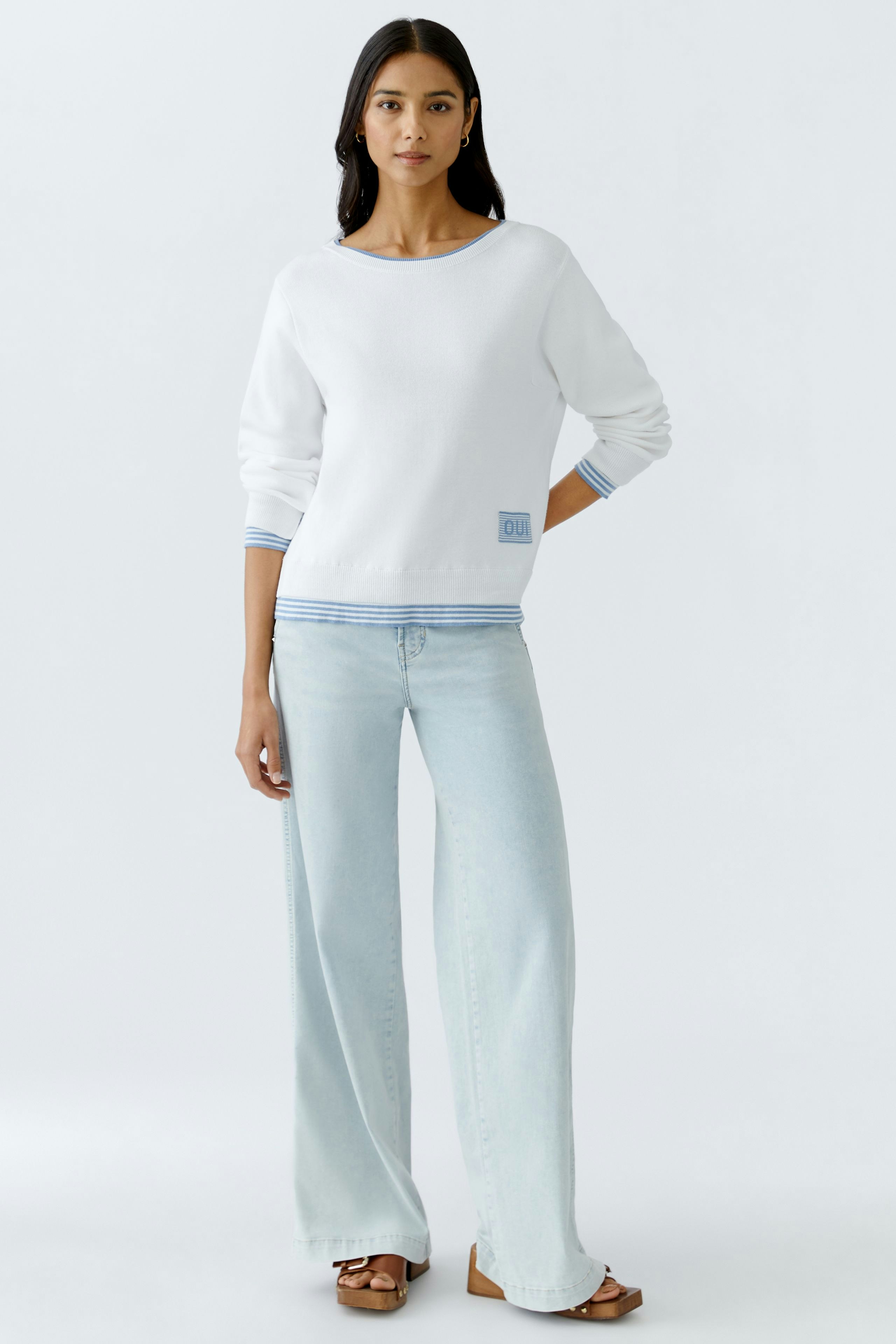 Stylish women's pullover: A woman in a white pullover with blue details, paired with light jeans.