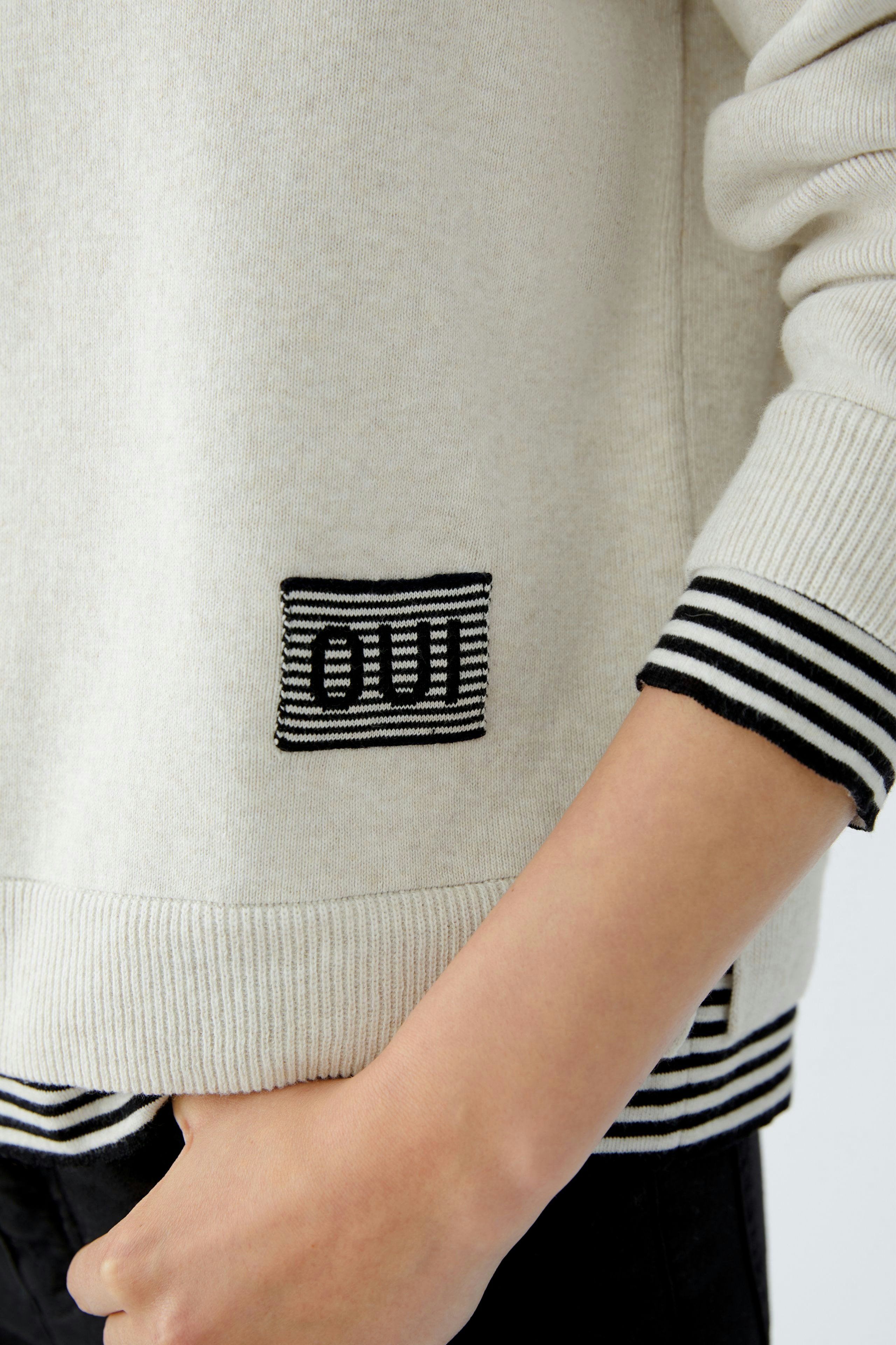 Modern women's pullover: A woman in a light beige pullover with a relaxed fit and minimalistic style.