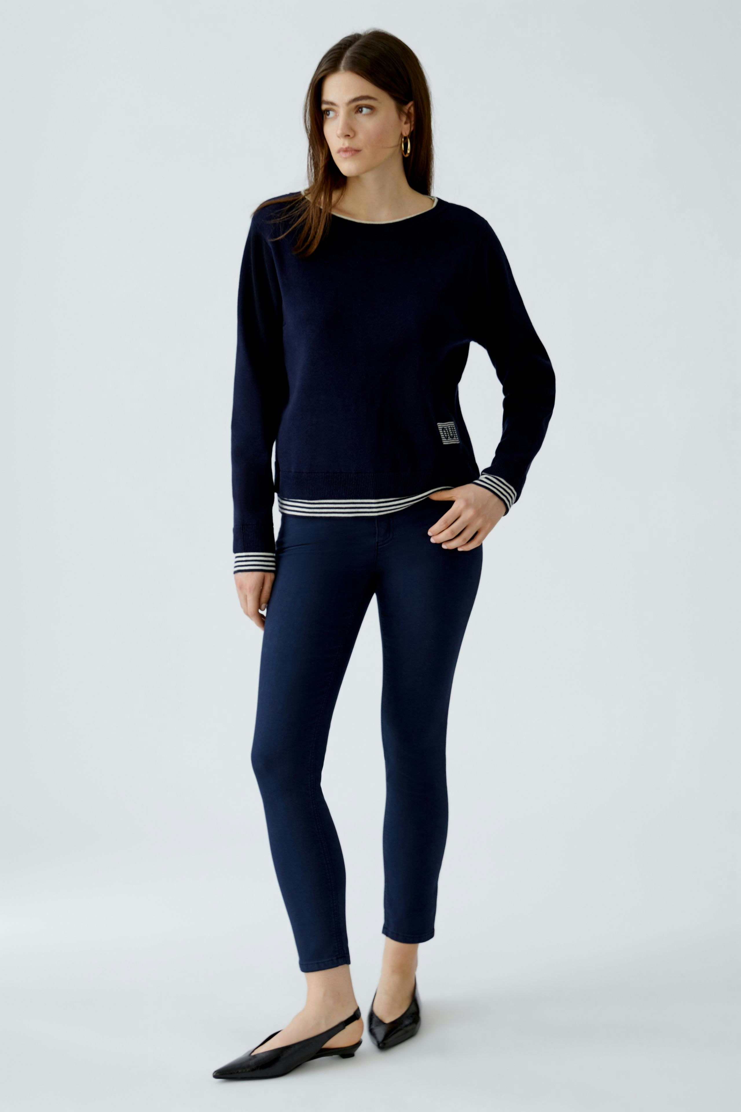 Modern women's pullover: A woman in a navy pullover with a casual striped shirt underneath.