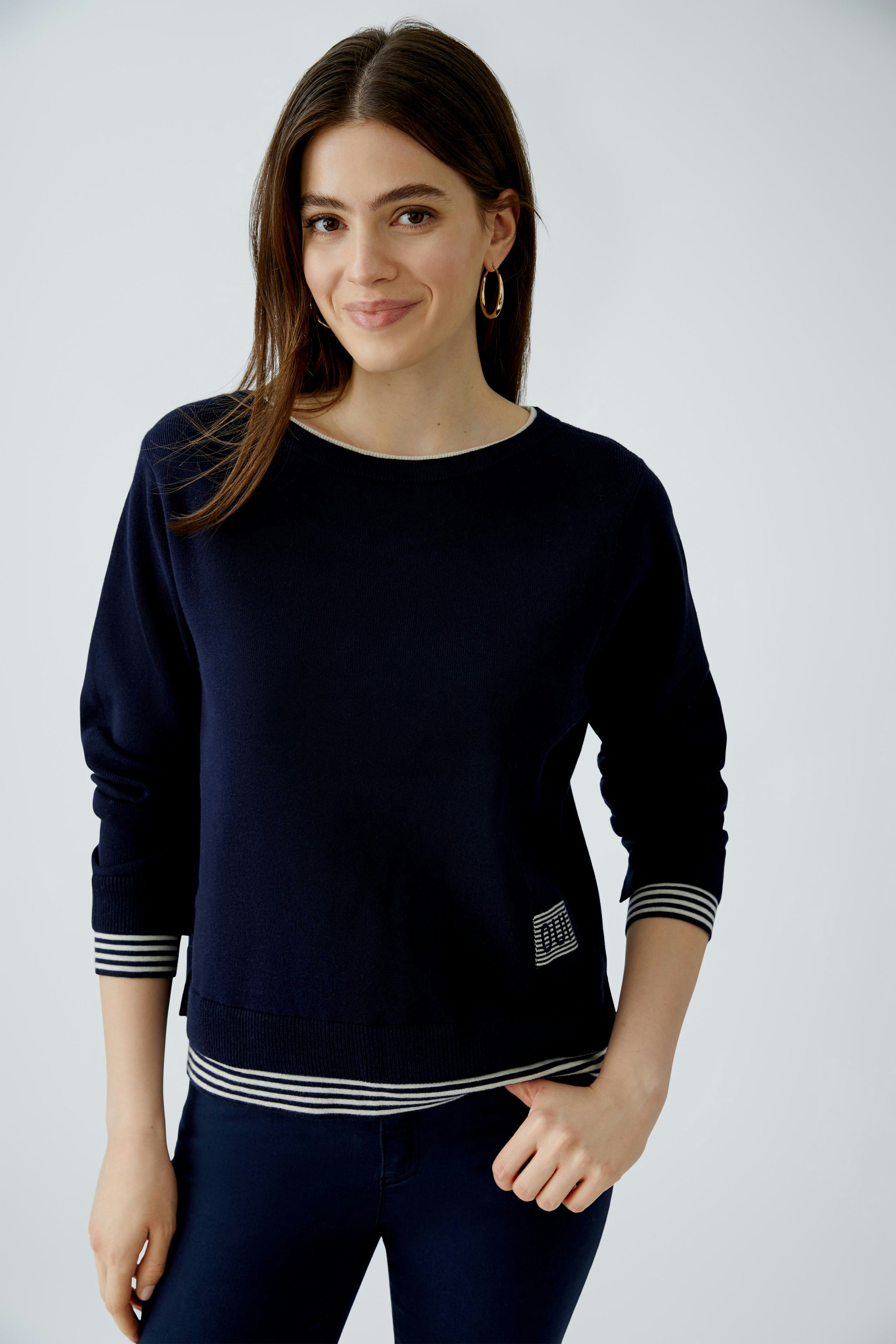Modern women's pullover: A woman in a navy pullover with striped cuffs smiles confidently.