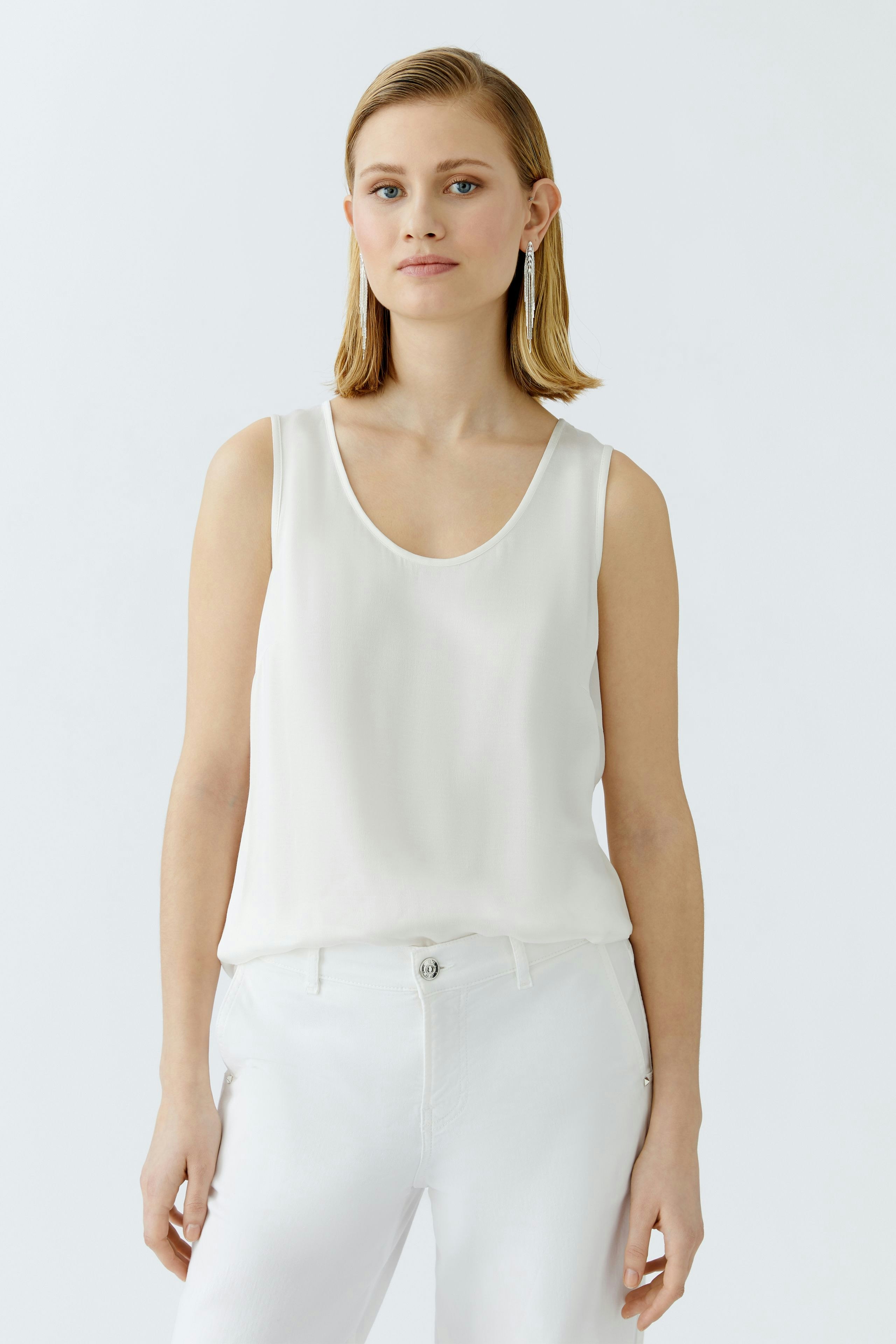 Elegant women's top: A woman in a white sleeveless top paired with casual jeans.