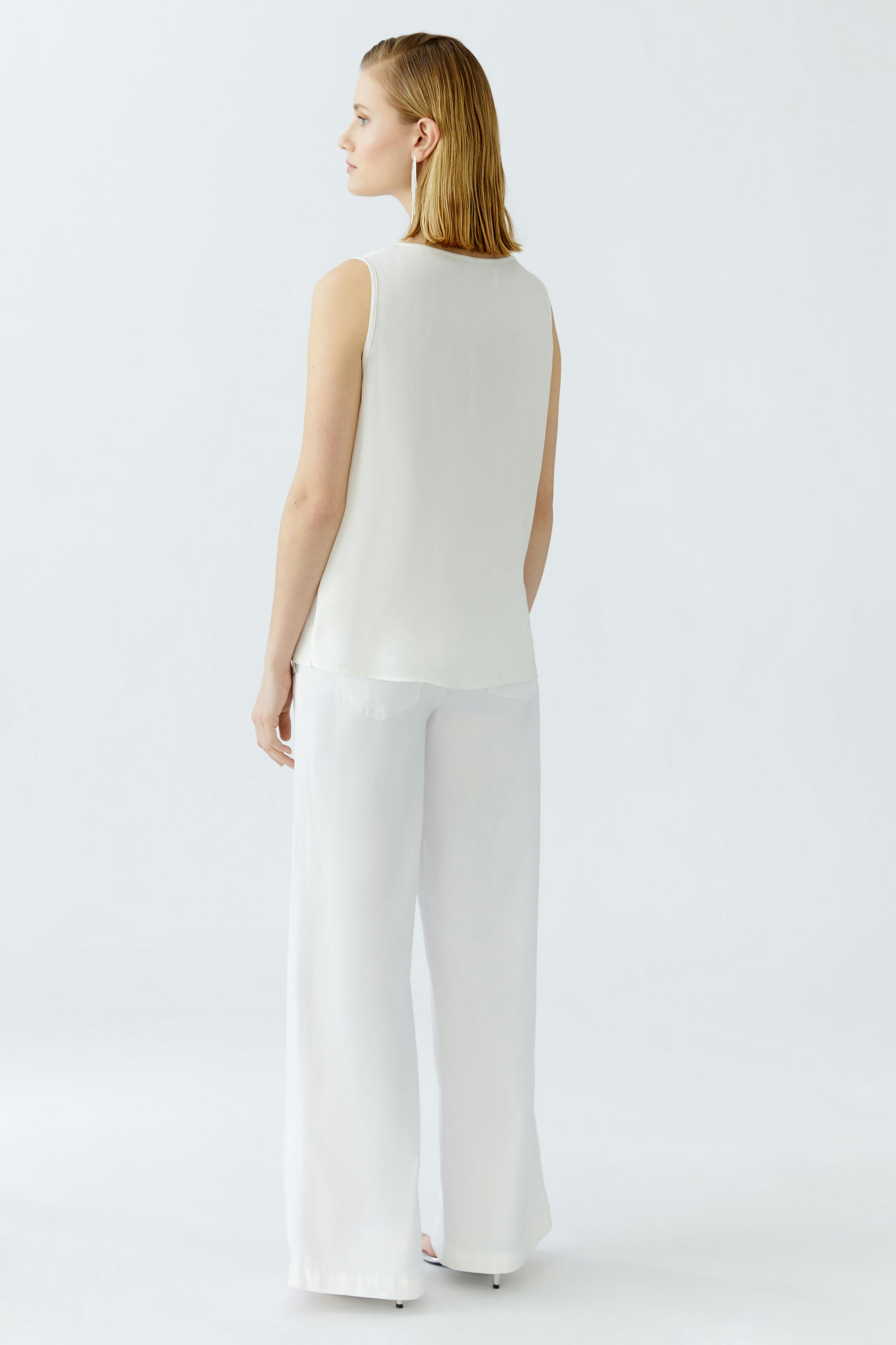 Elegant women's top: A woman in a light sleeveless top paired with wide-leg jeans.