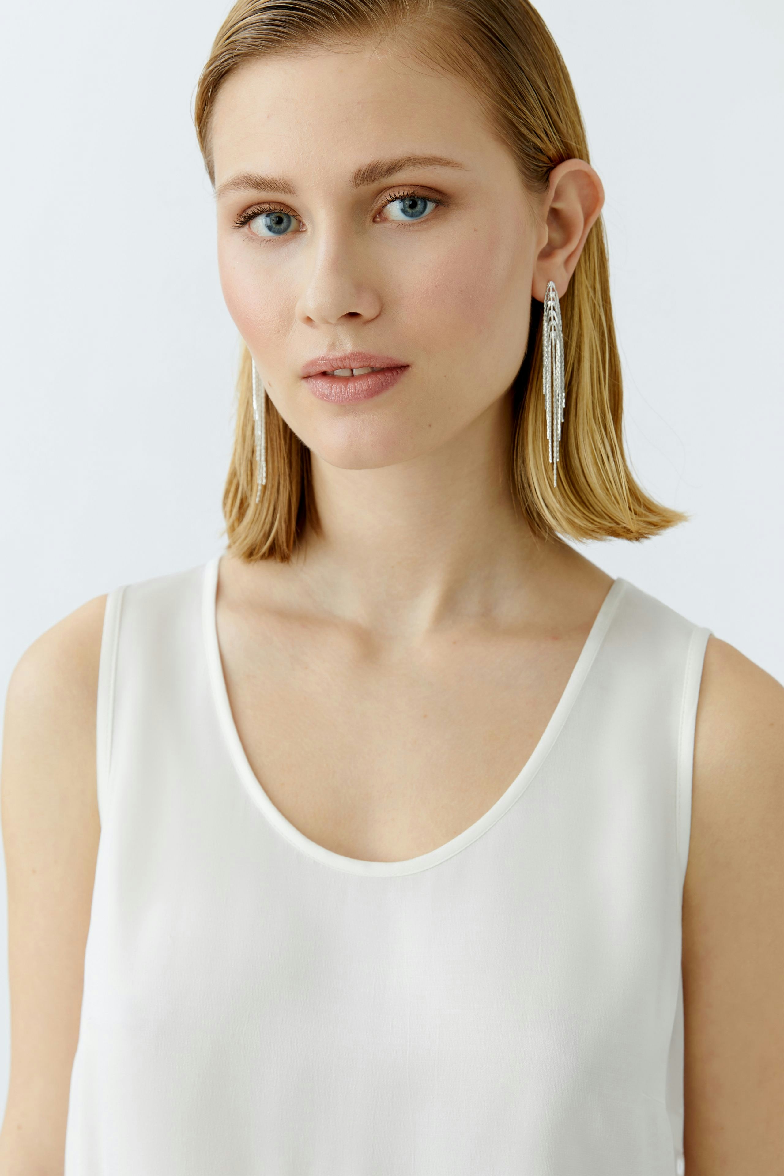 Elegant women's top: A woman in a light, sleeveless top with a scoop neckline, exuding effortless style.