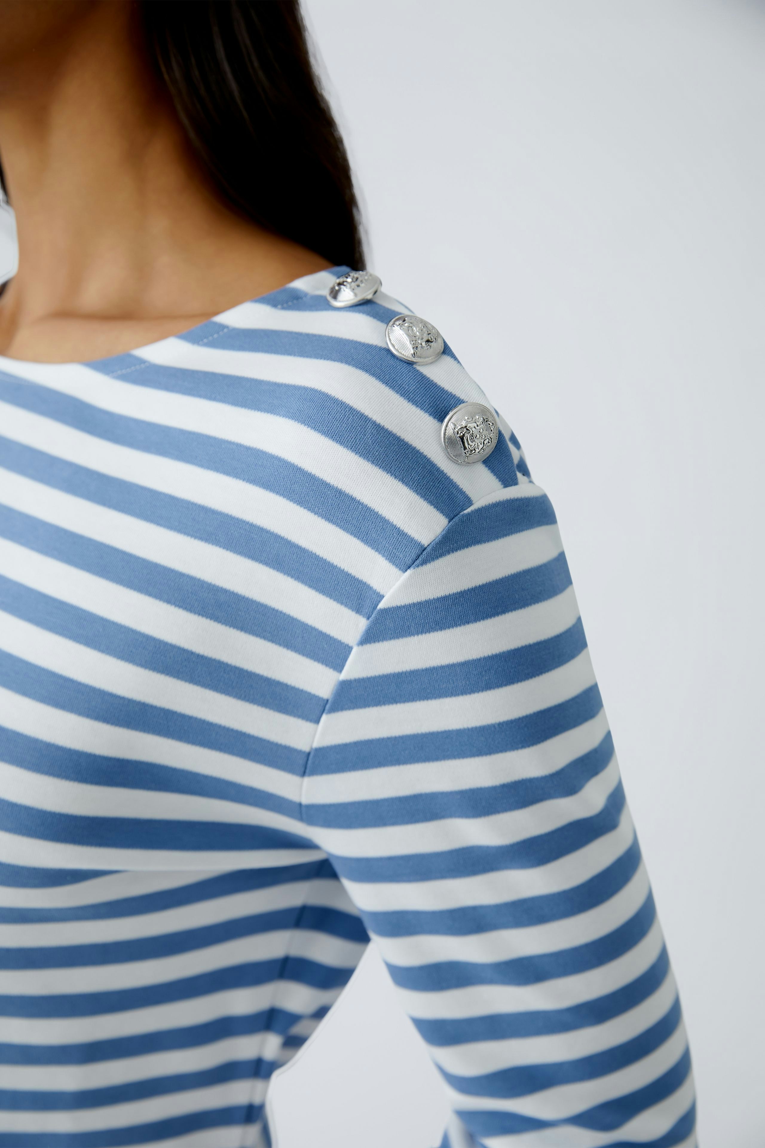 Stylish long-sleeve shirt: Woman in a blue and white striped pullover with decorative buttons.