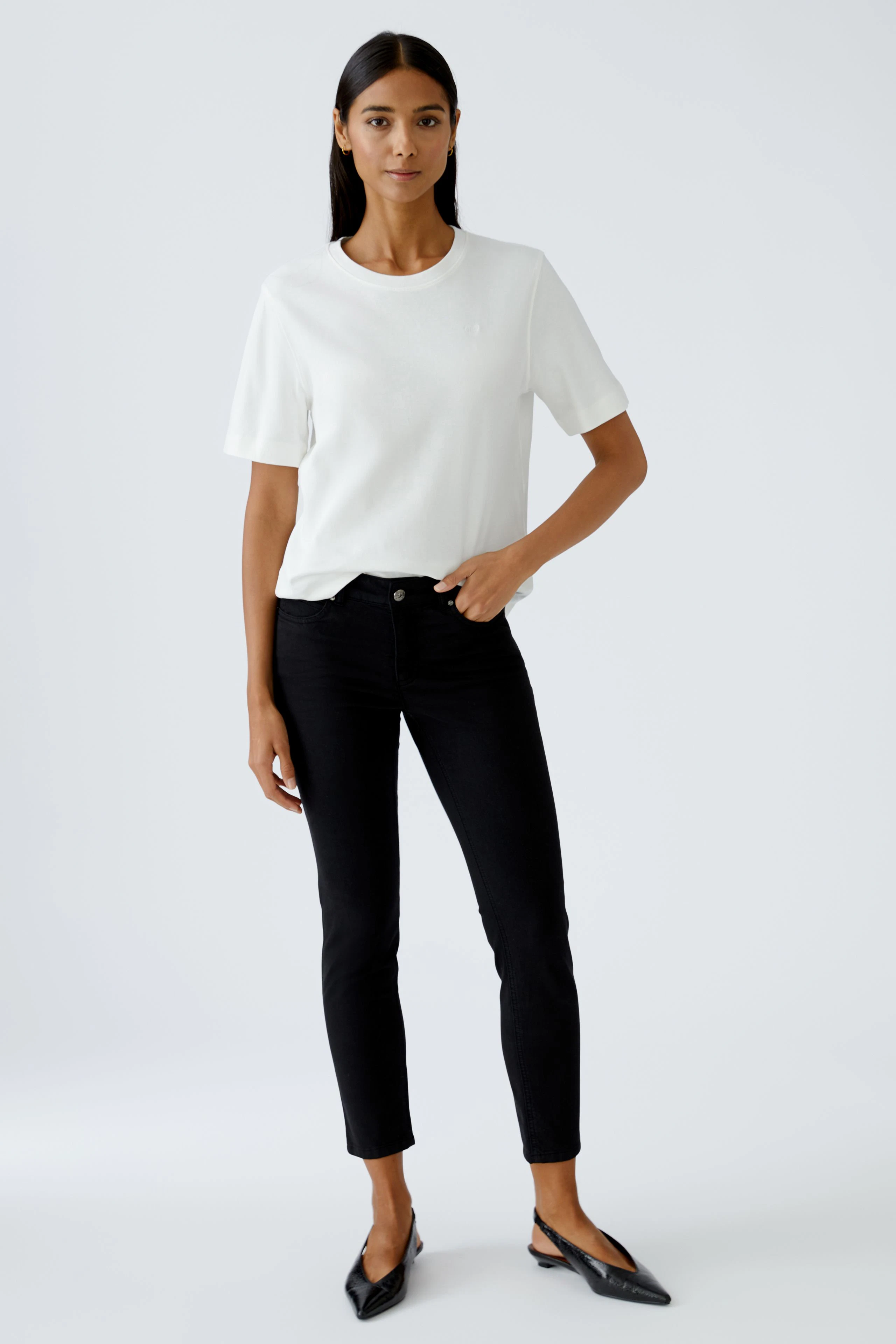 Damen-T-Shirt: Frau in weißem T-Shirt und schwarzen Jeans steht lässig mit einer Hand in der Hosentasche.