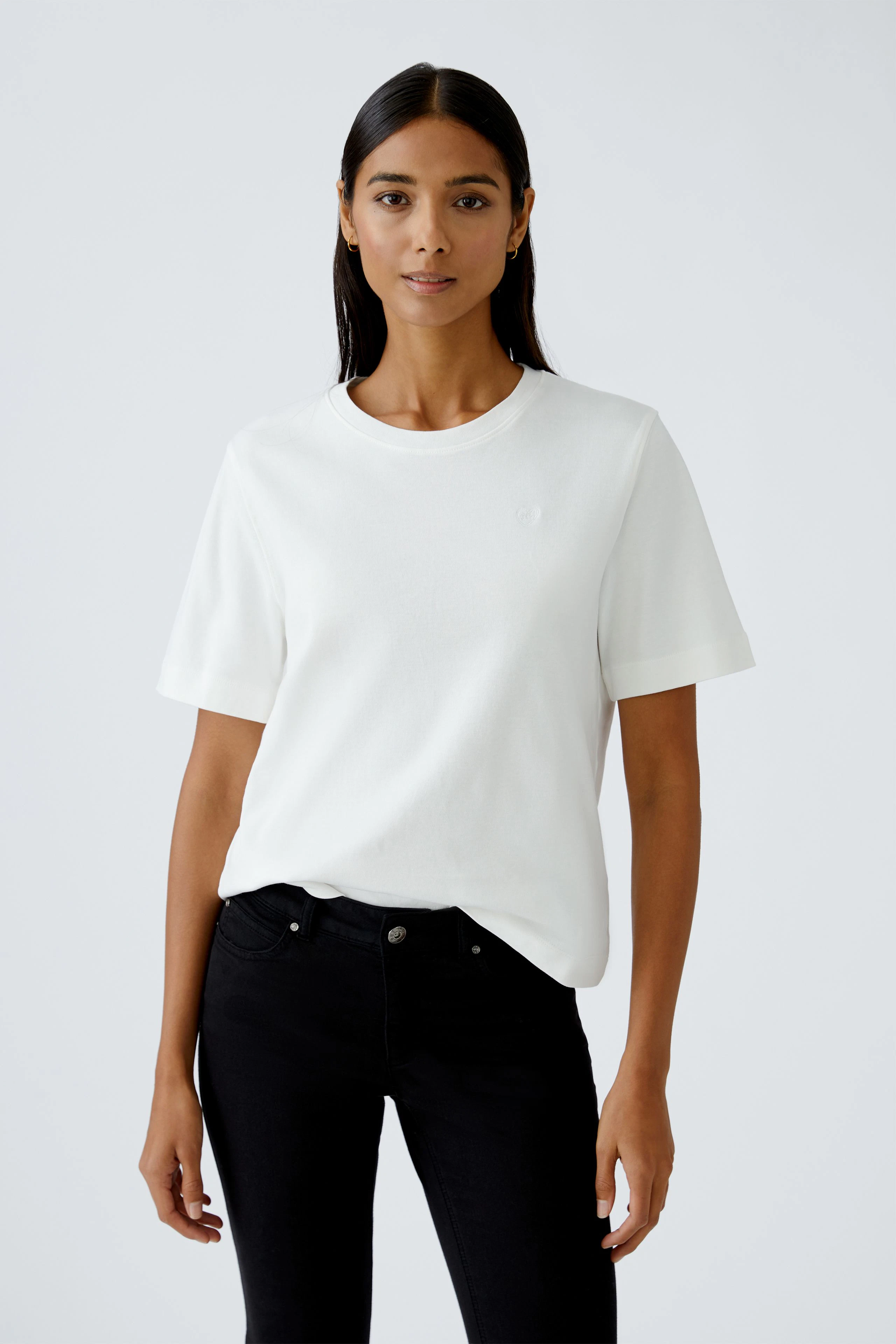 Damen-T-Shirt: Frau trägt ein schlichtes, weißes T-Shirt mit kurzen Ärmeln und lässiger Passform.