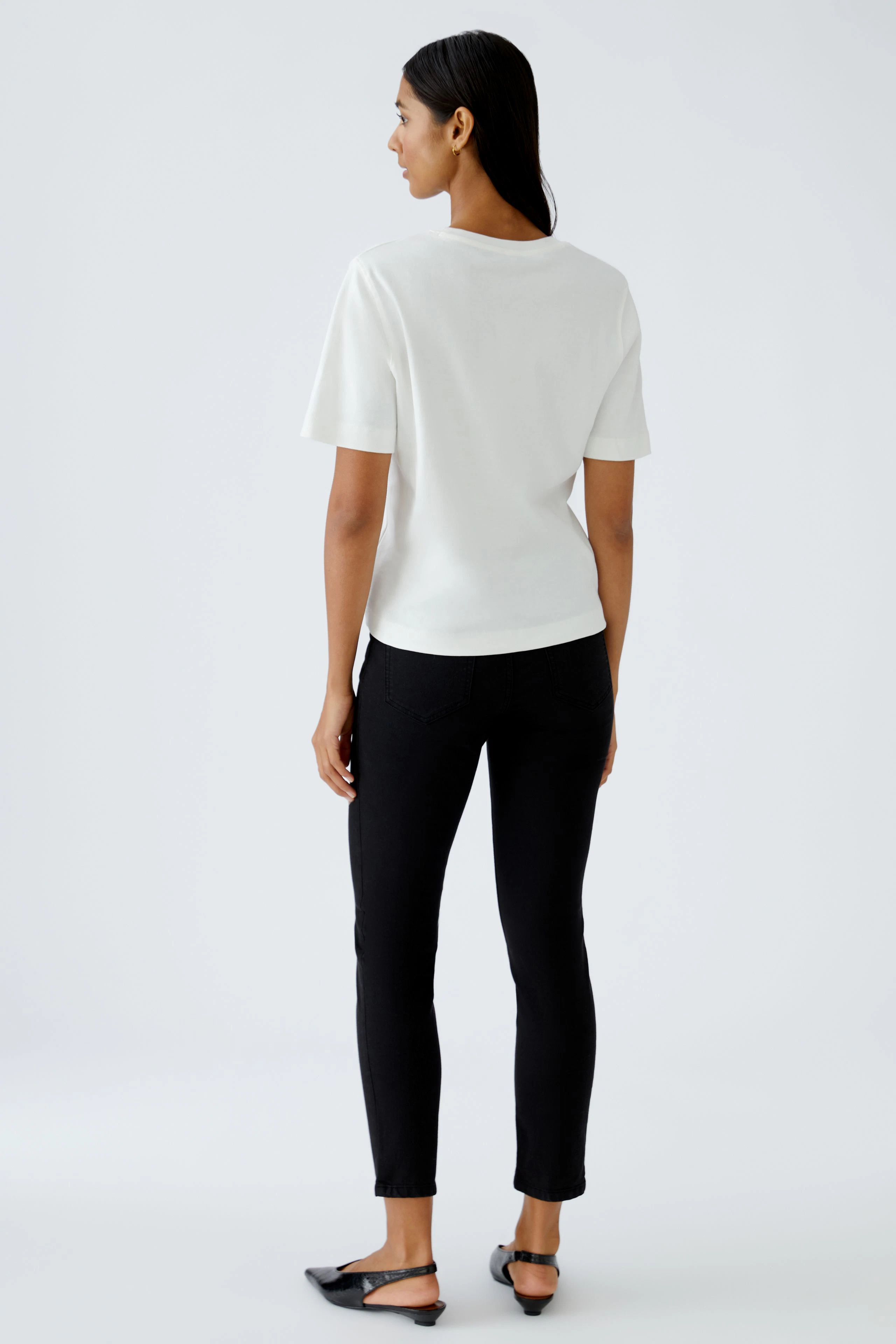 Bequeme Damen-T-Shirt: Frau in weißem T-Shirt und schwarzen Jeans steht entspannt mit dem Rücken zur Kamera.