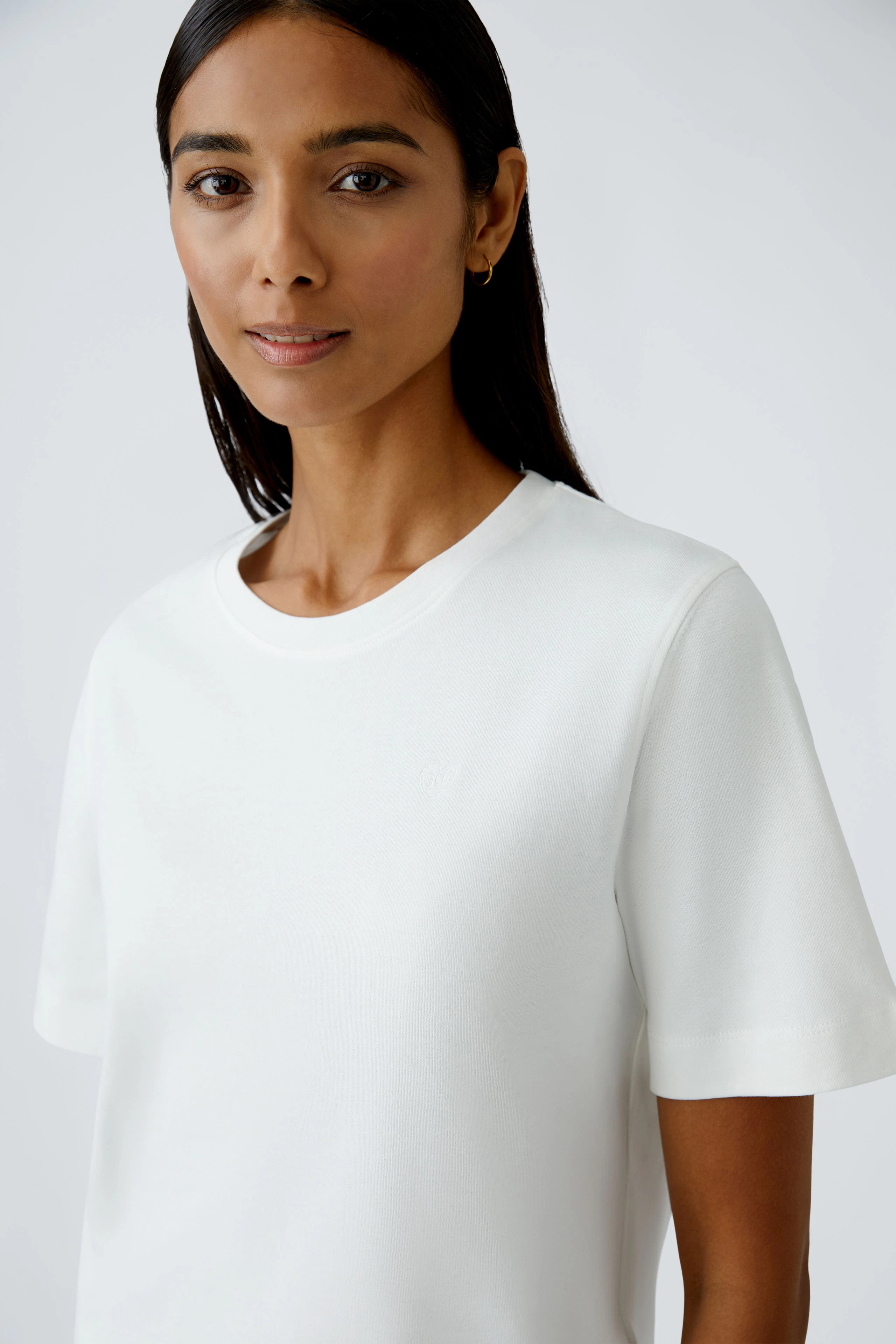Damen-T-Shirt: Frau trägt ein schlichtes, weißes T-Shirt mit kurzen Ärmeln und Rundhalsausschnitt.