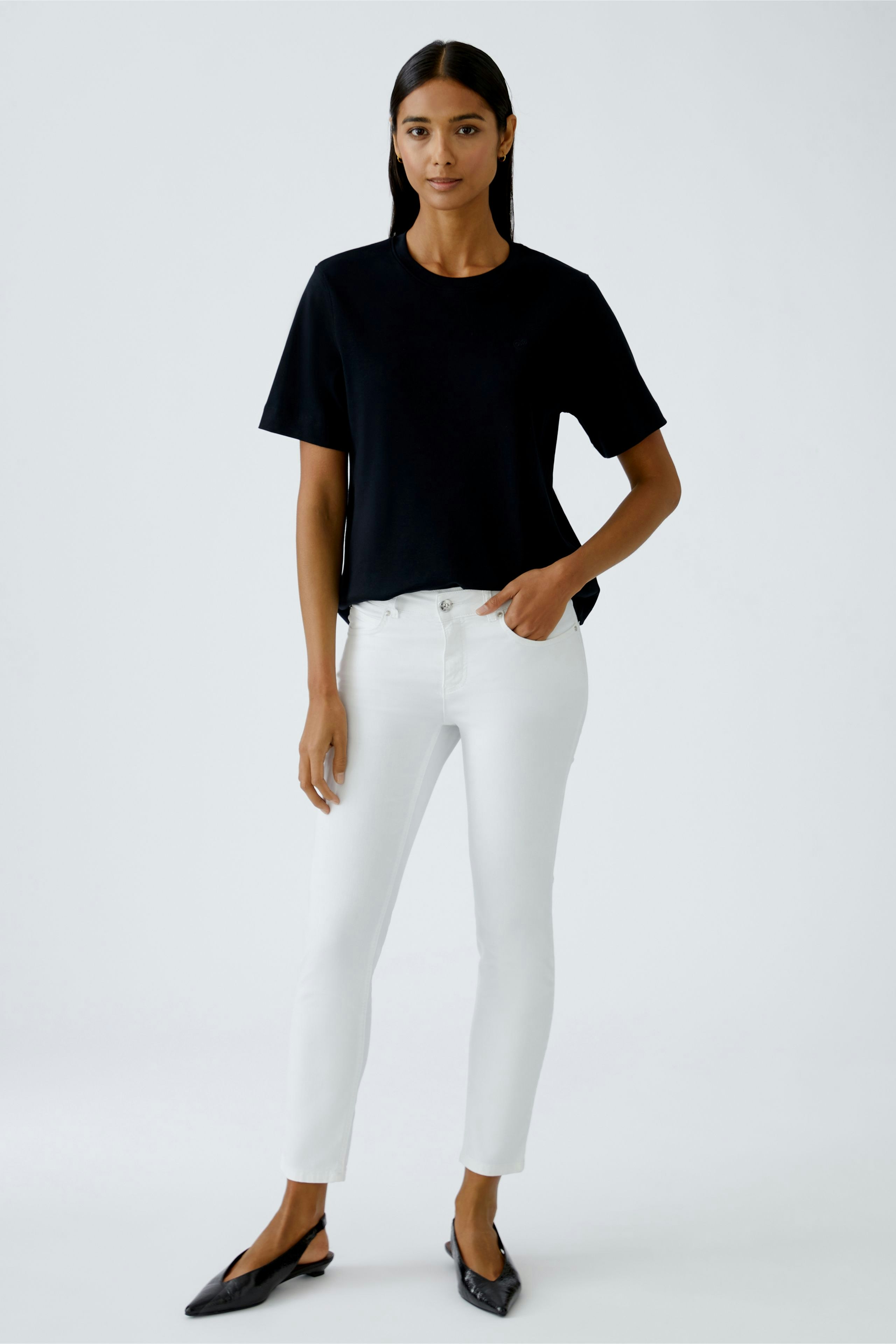 Schwarzes Damen-T-Shirt: Frau trägt lässiges T-Shirt mit kurzen Ärmeln und weißen Jeans.