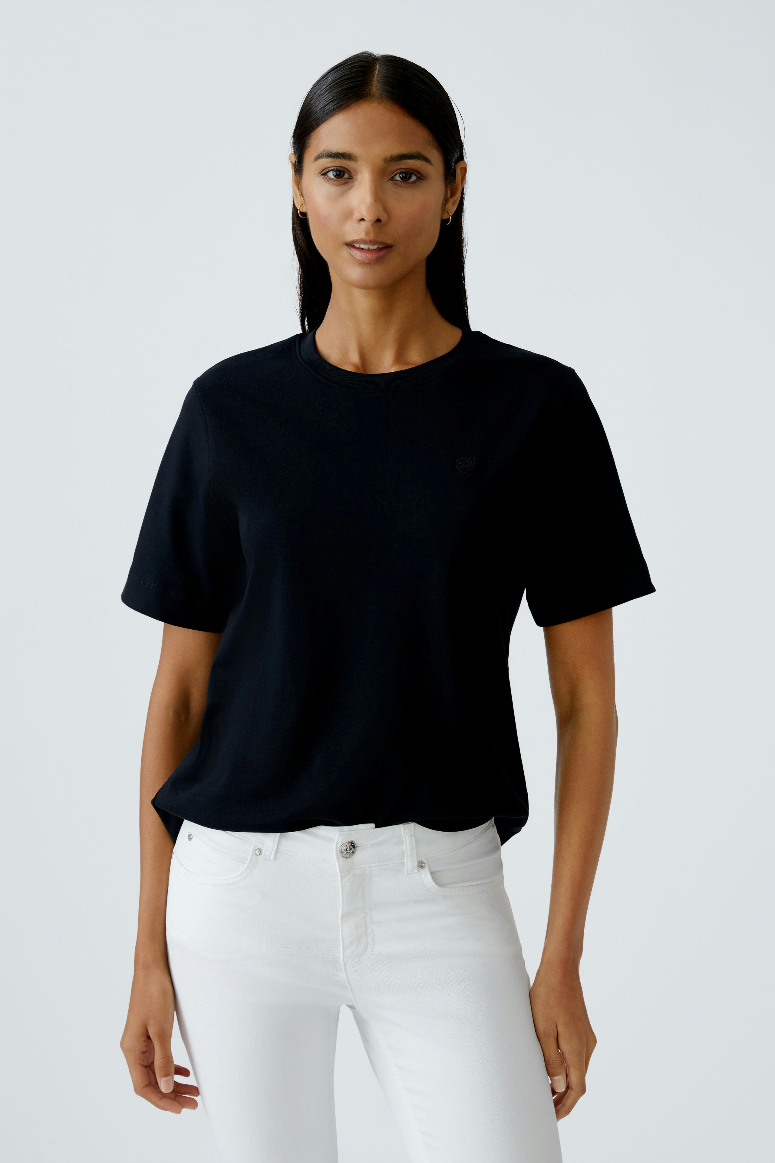 Schwarzes Damen-T-Shirt: Frau trägt ein schlichtes T-Shirt mit kurzen Ärmeln und lässigen weißen Jeans.