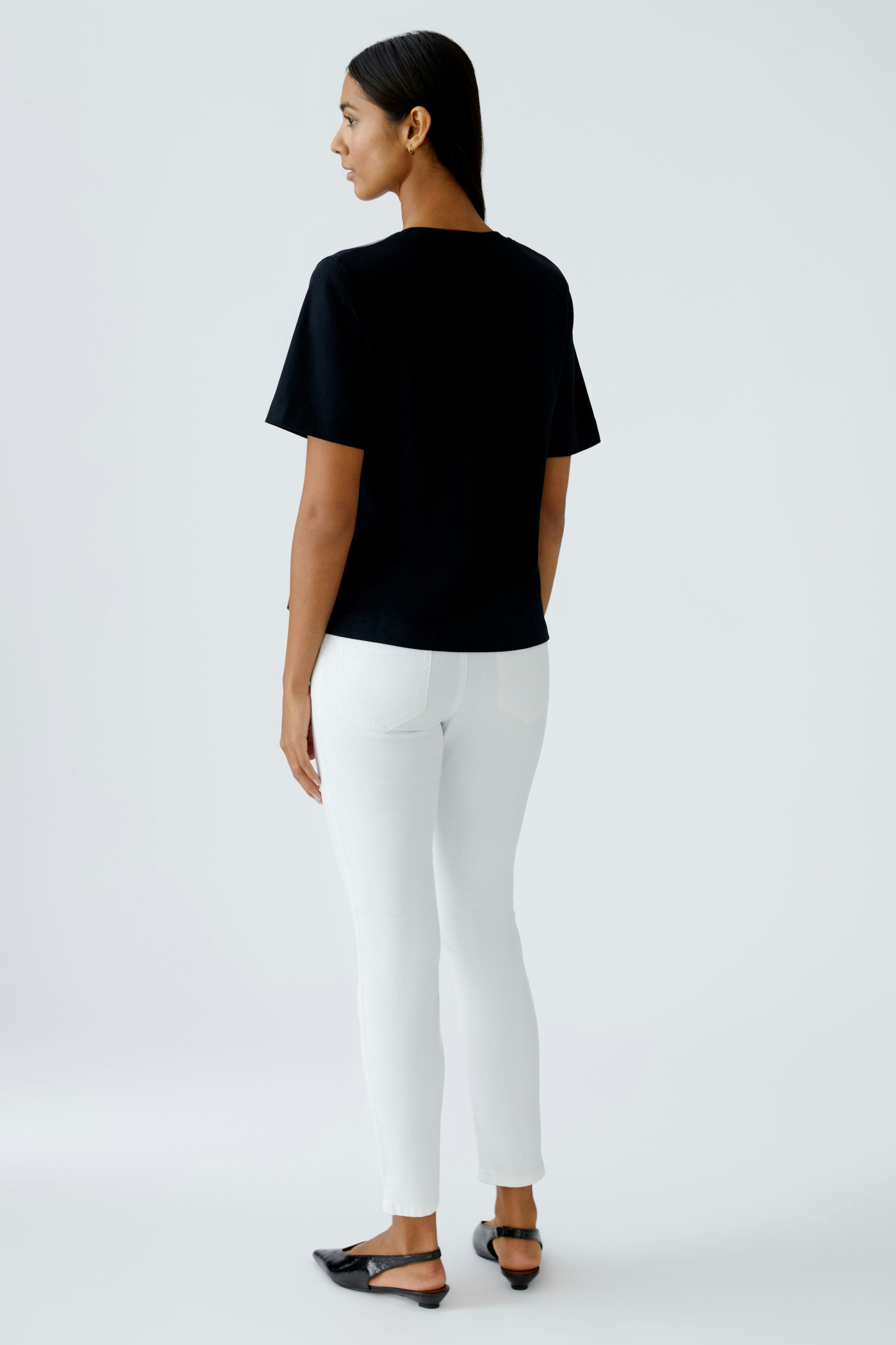 Schwarzes Damen-T-Shirt: Frau mit kurzem Ärmel und lässigem Schnitt, kombiniert mit weißen Jeans.