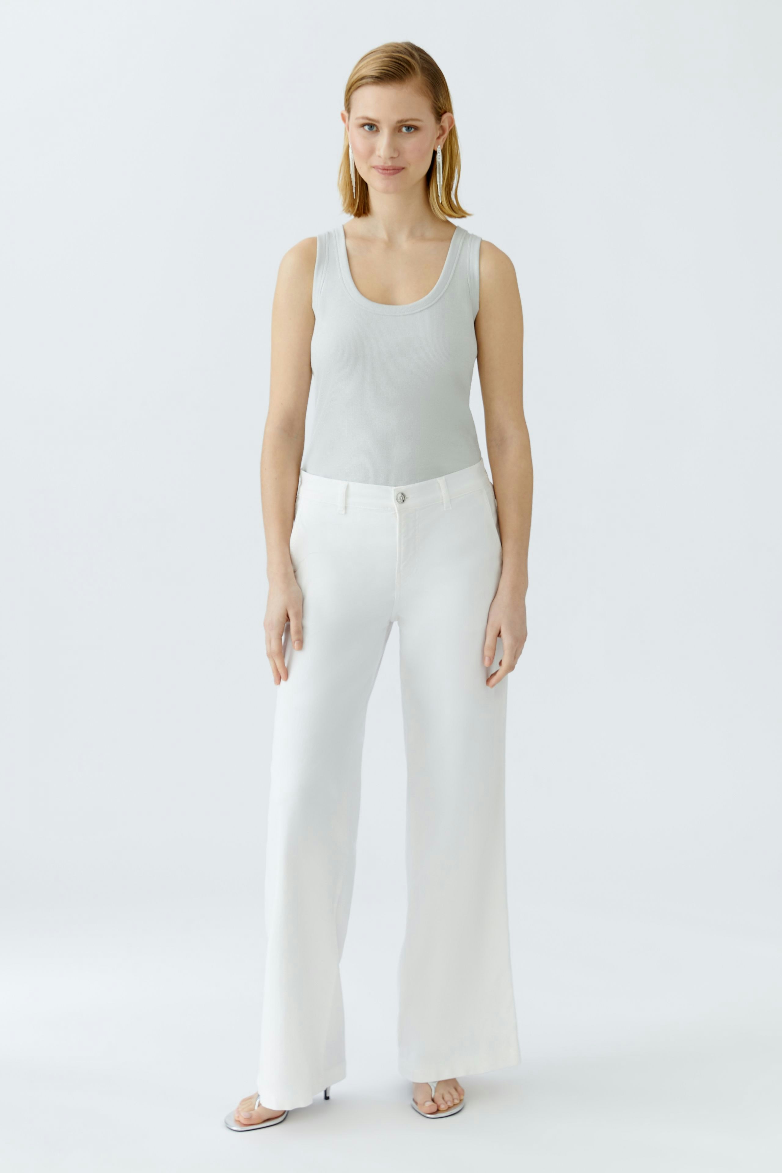 Casual women's top: A woman in a light gray tank top paired with wide white pants stands confidently.