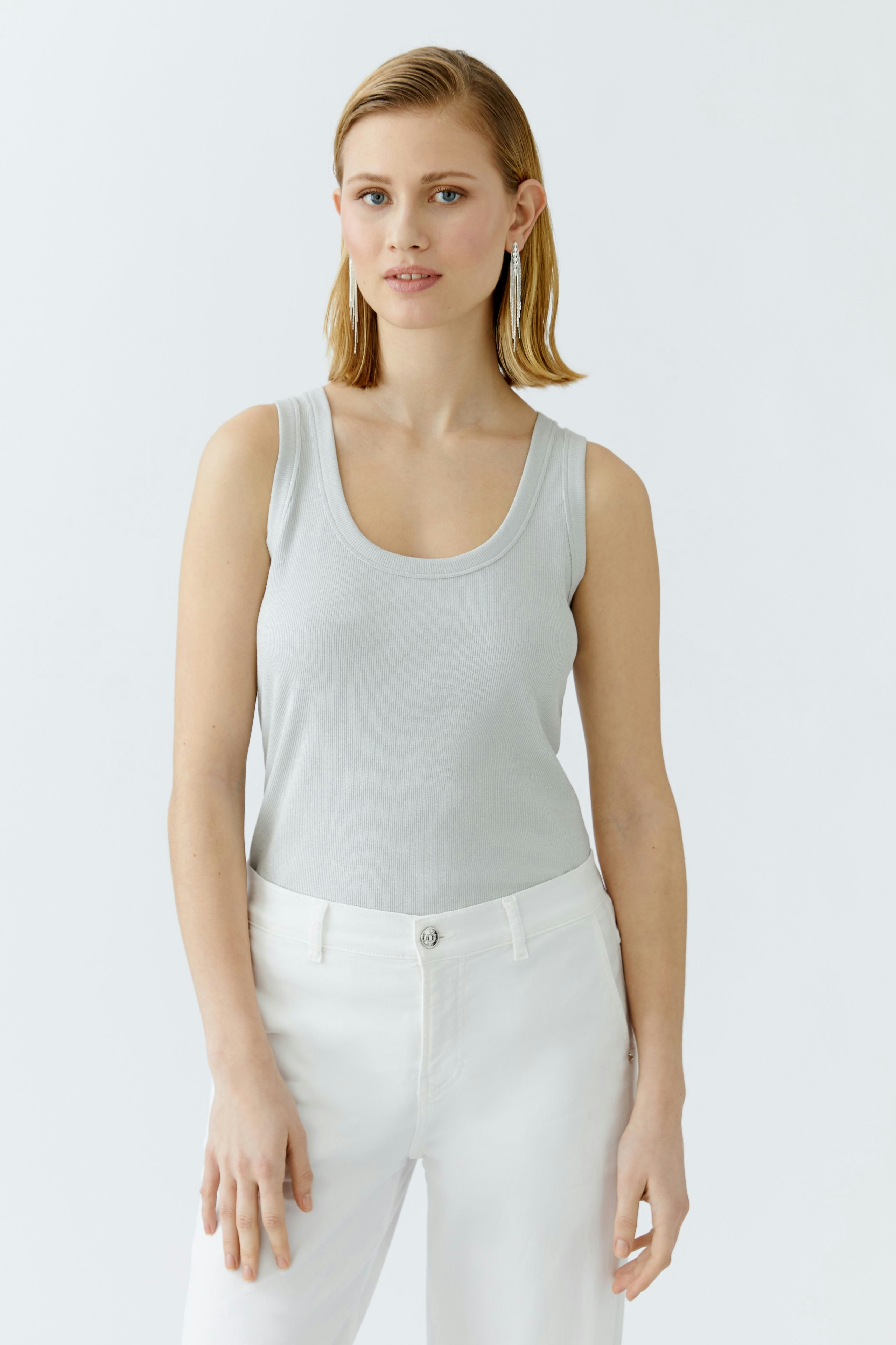 Casual women's top: Young woman in a light gray tank top paired with white pants, looking relaxed.