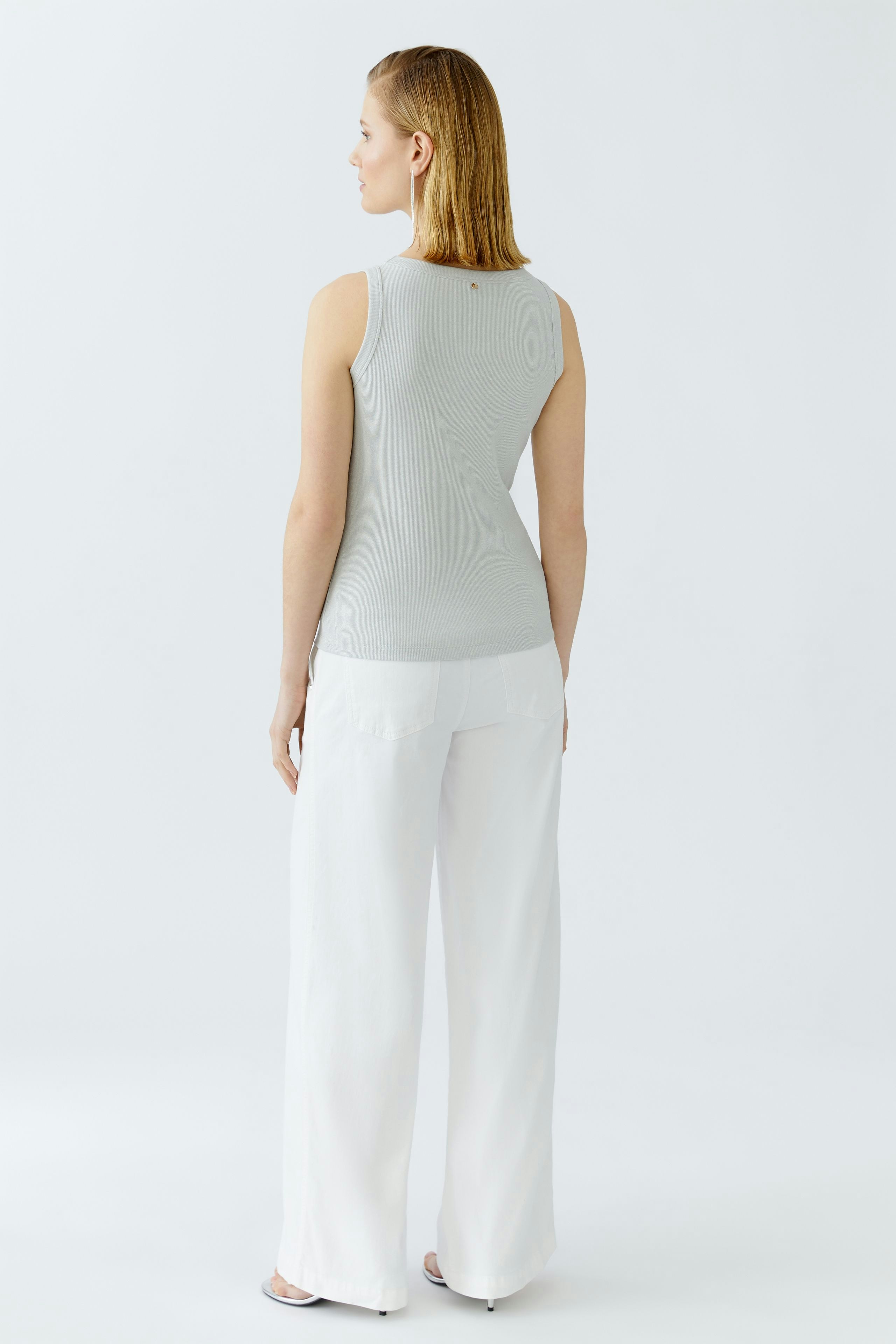 Casual women's top: A woman in a light gray sleeveless top paired with white wide-leg pants.