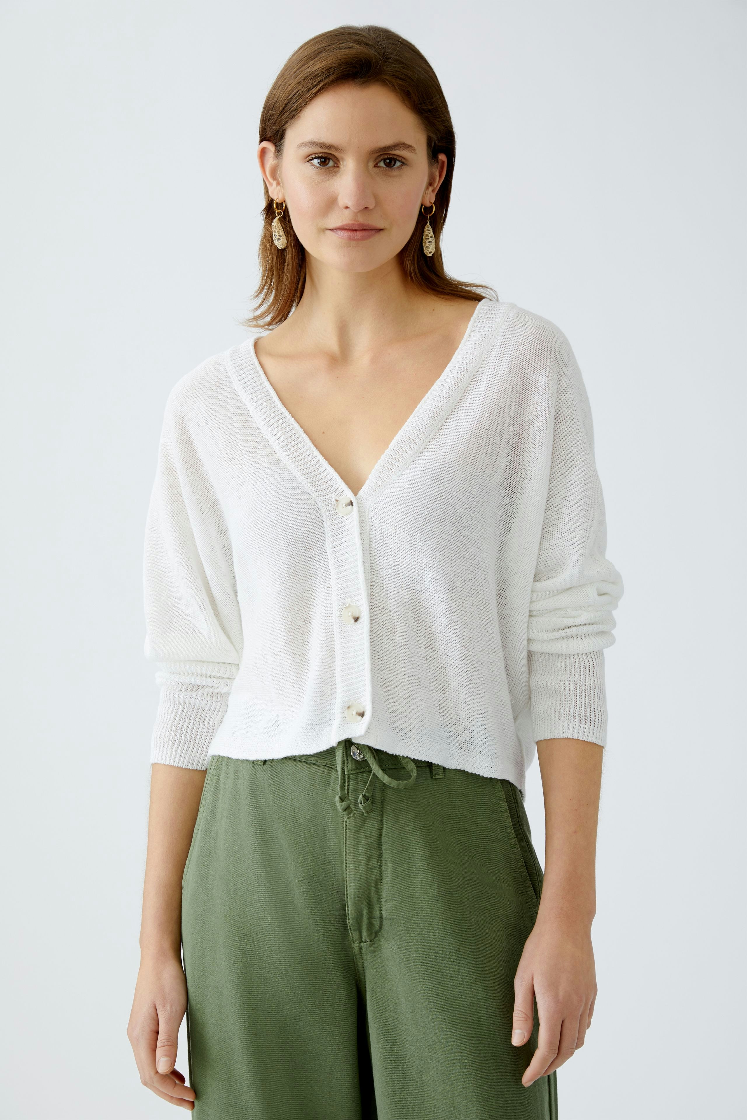 Lightweight women's cardigan: A woman in a white cardigan with buttons and relaxed green pants.