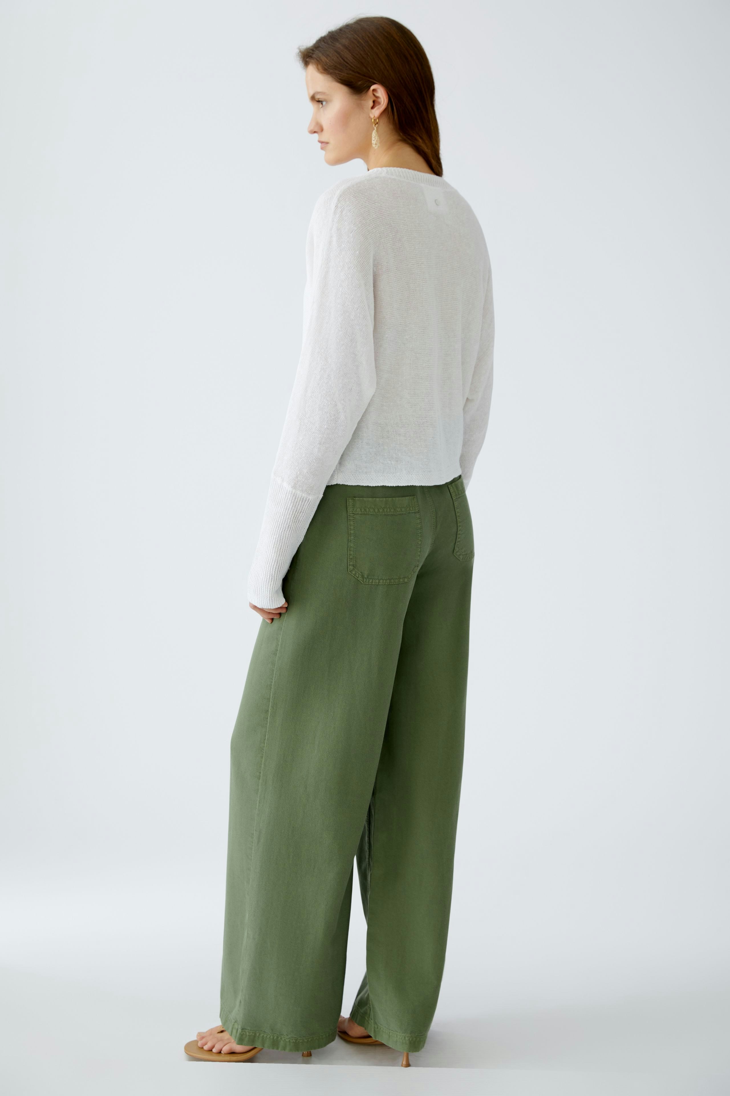 Stylish women's cardigan: A woman in a light cardigan paired with wide green pants, showcasing a relaxed look.