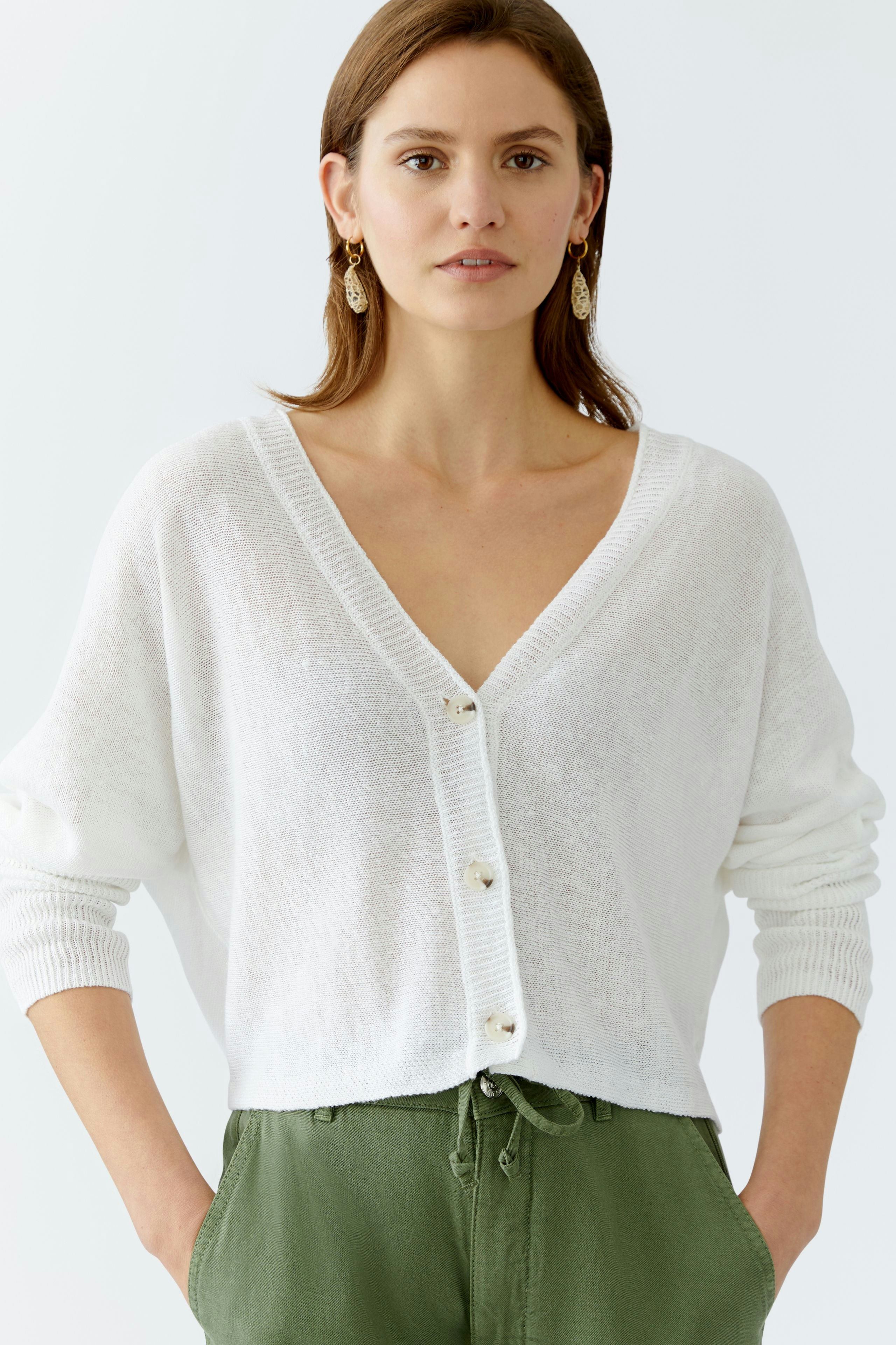 Stylish women's cardigan: A woman in a white cardigan with a V-neck and buttons, paired with green pants.