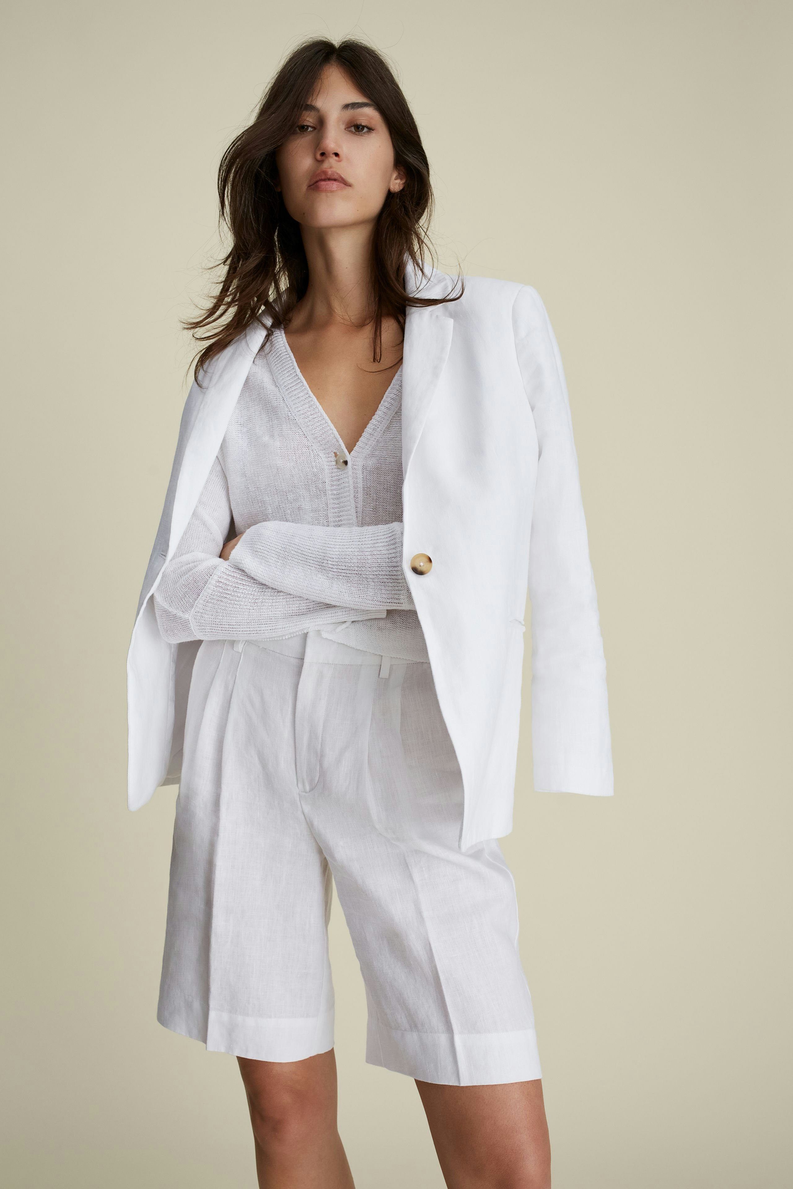 Chic women's cardigan: A woman in a white cardigan layered over a light top and tailored shorts.
