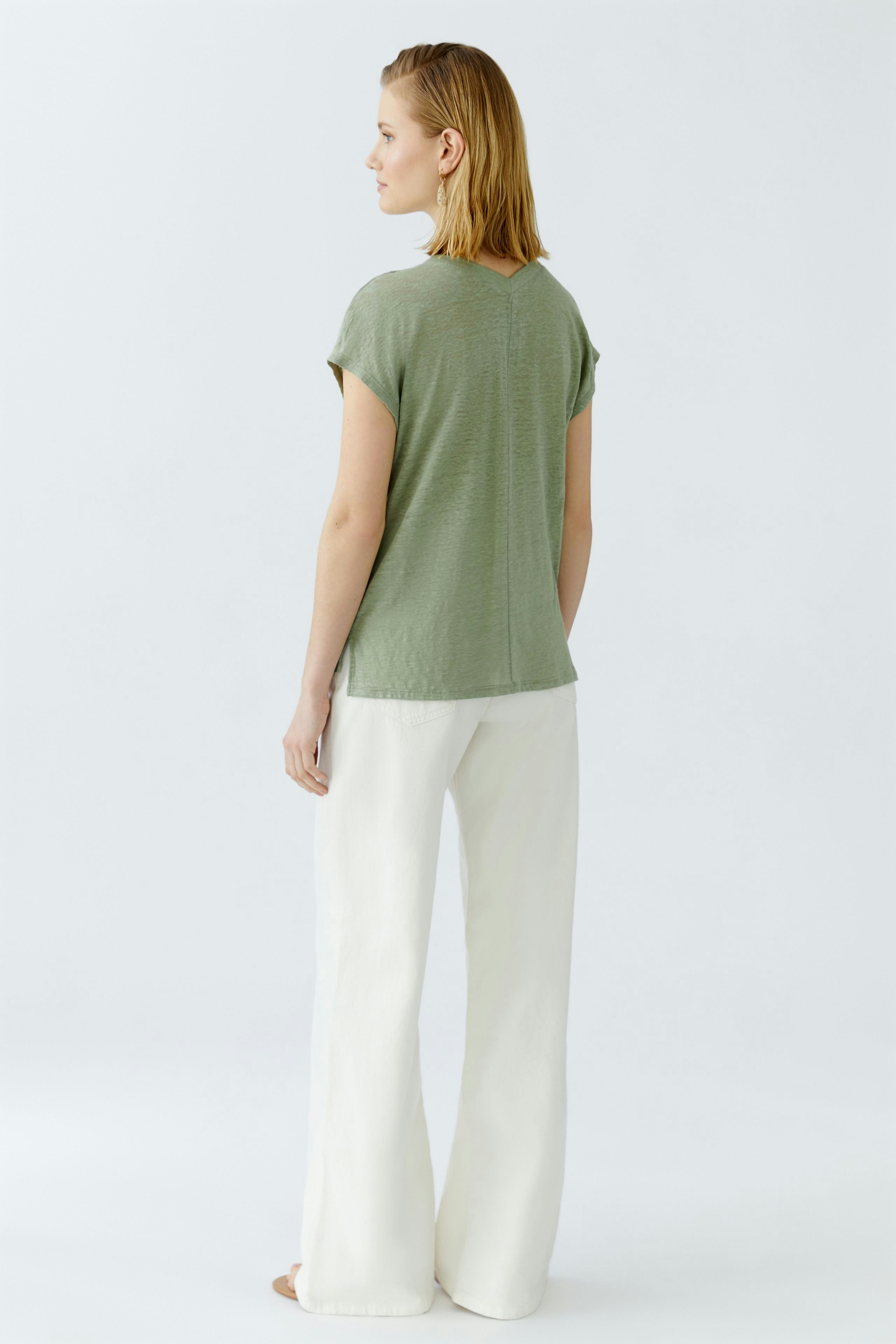 Damen-T-Shirt: Frau in lässigem, grünem T-Shirt mit kurzen Ärmeln und weiten, weißen Hosen.