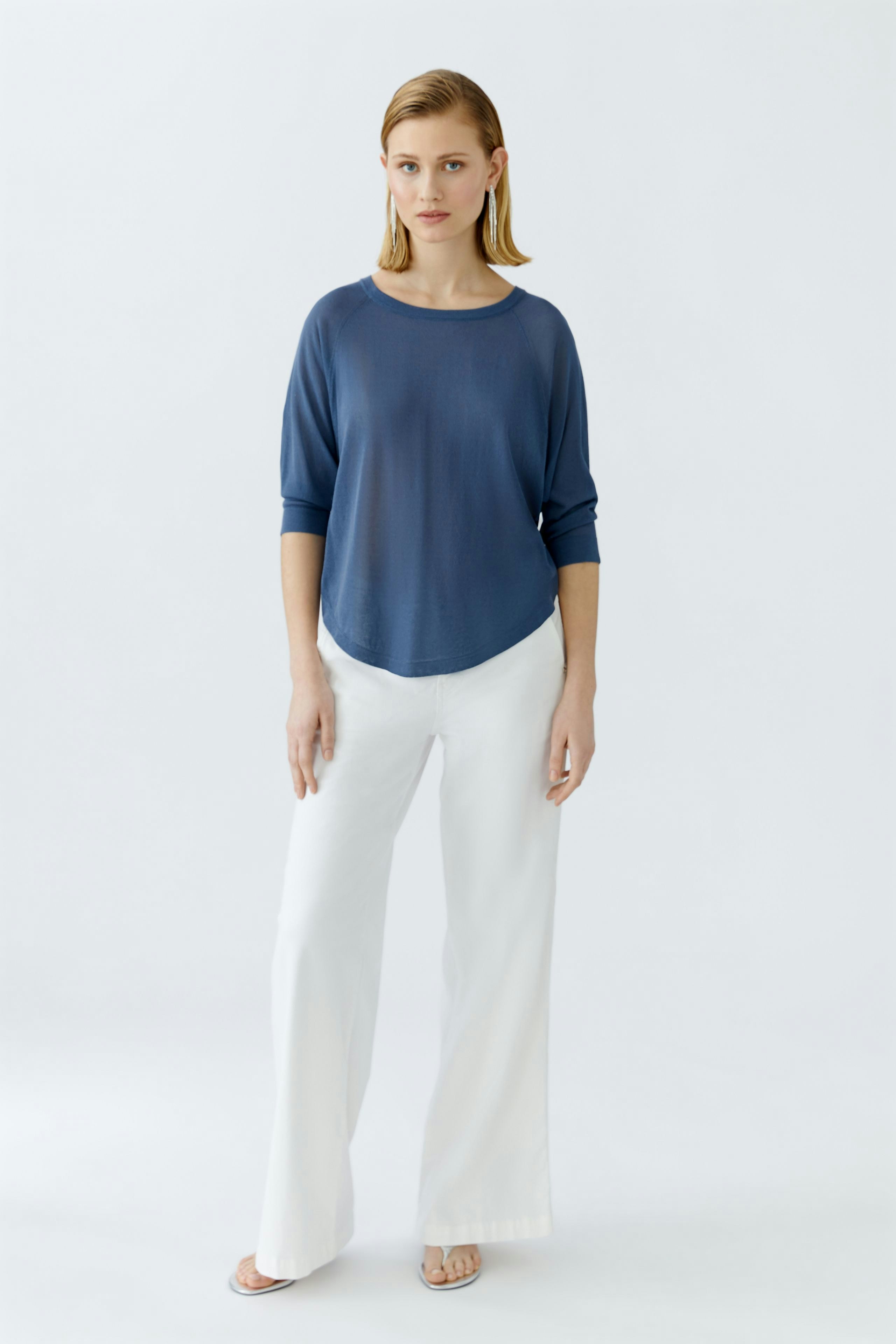 Damen-Pullover: Junge Frau in blauem, lässigem Pullover mit weitem Schnitt und weißen, weiten Hosen.