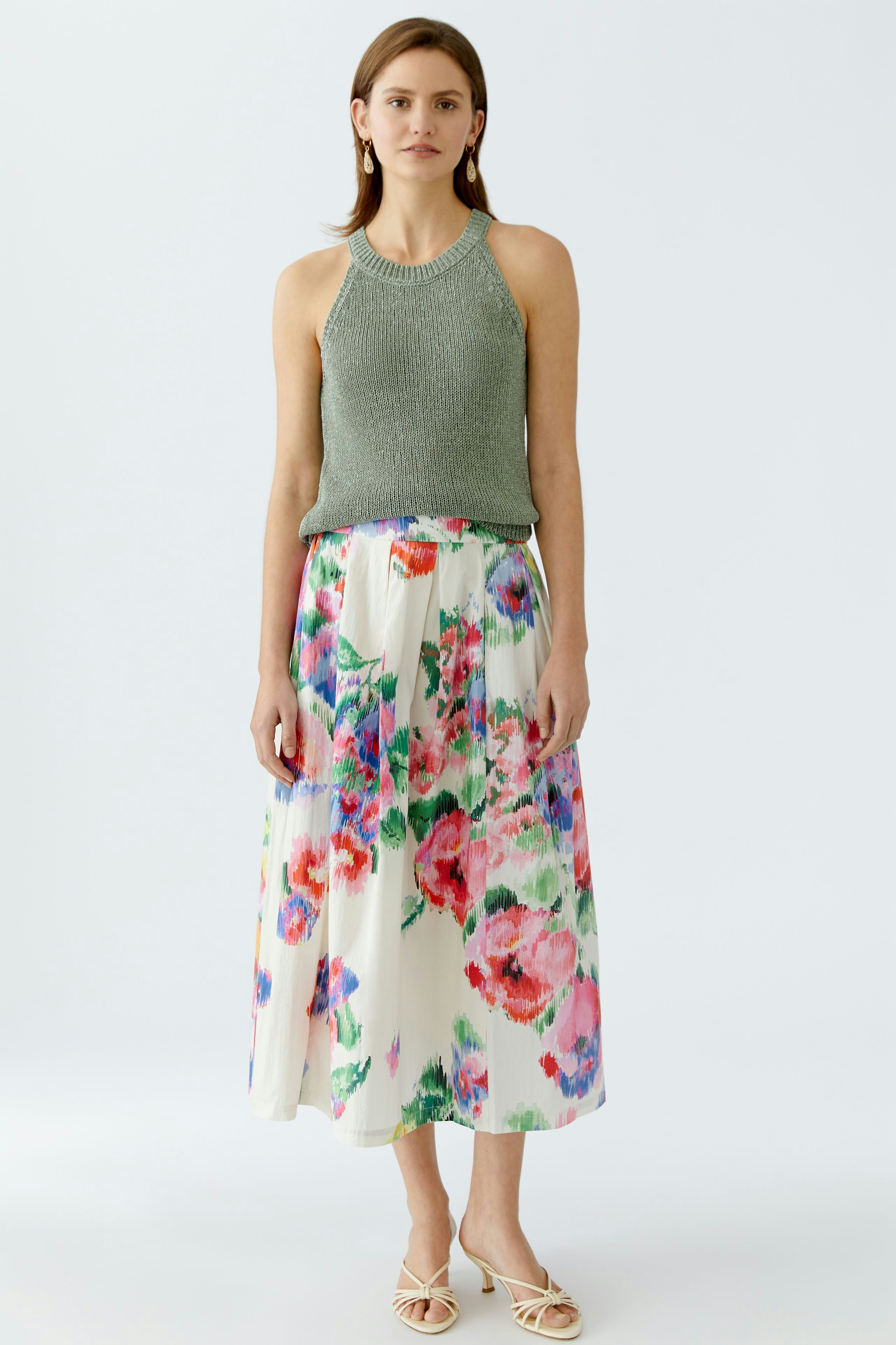 Elegantes Damen-Top: Frau in einem grünen Top mit floralem Rock, ideal für frühlingshafte Anlässe.