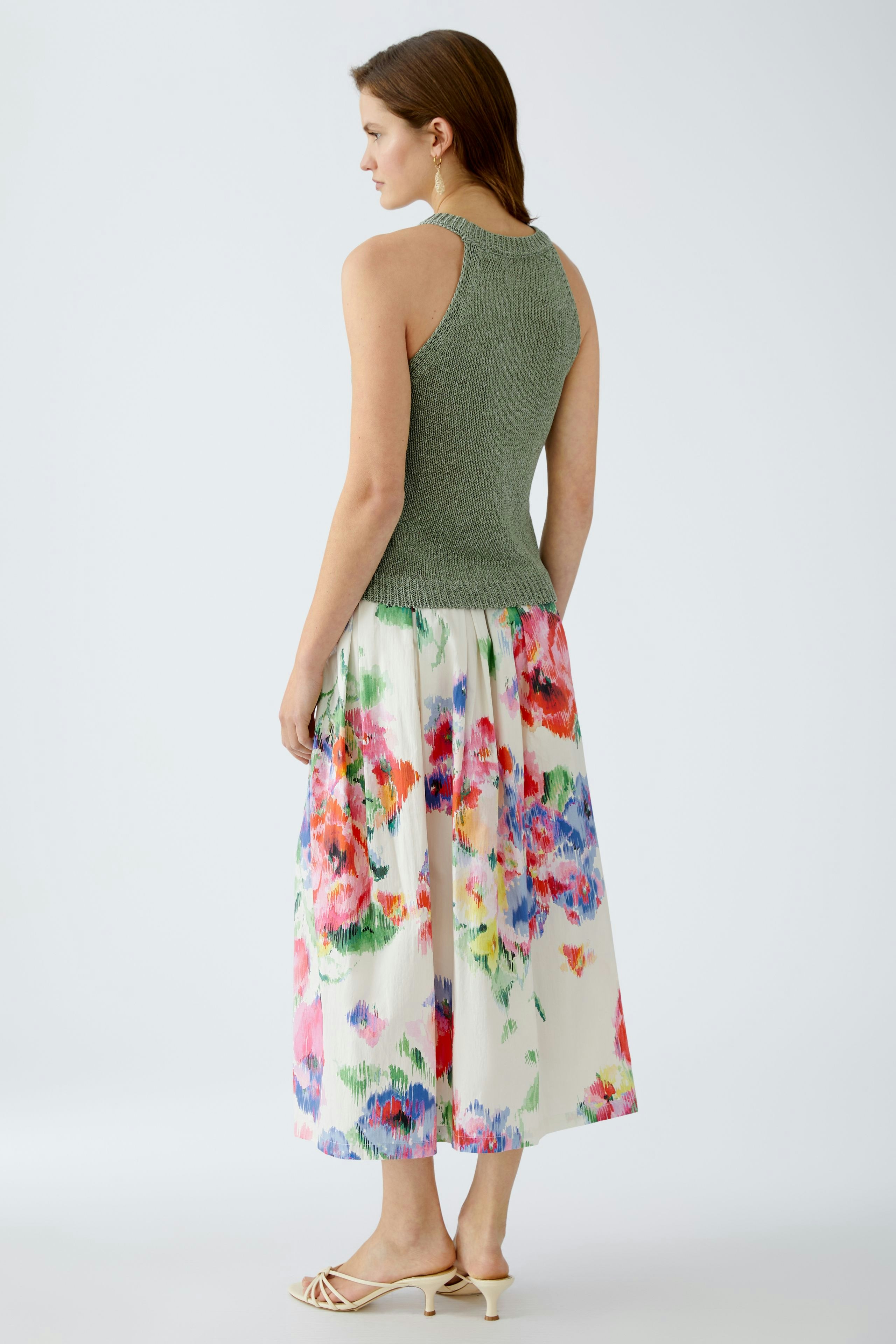 Elegantes Damen-Top: Frau in grünem Top mit Rückenausschnitt und farbenfrorem, floralem Rock.