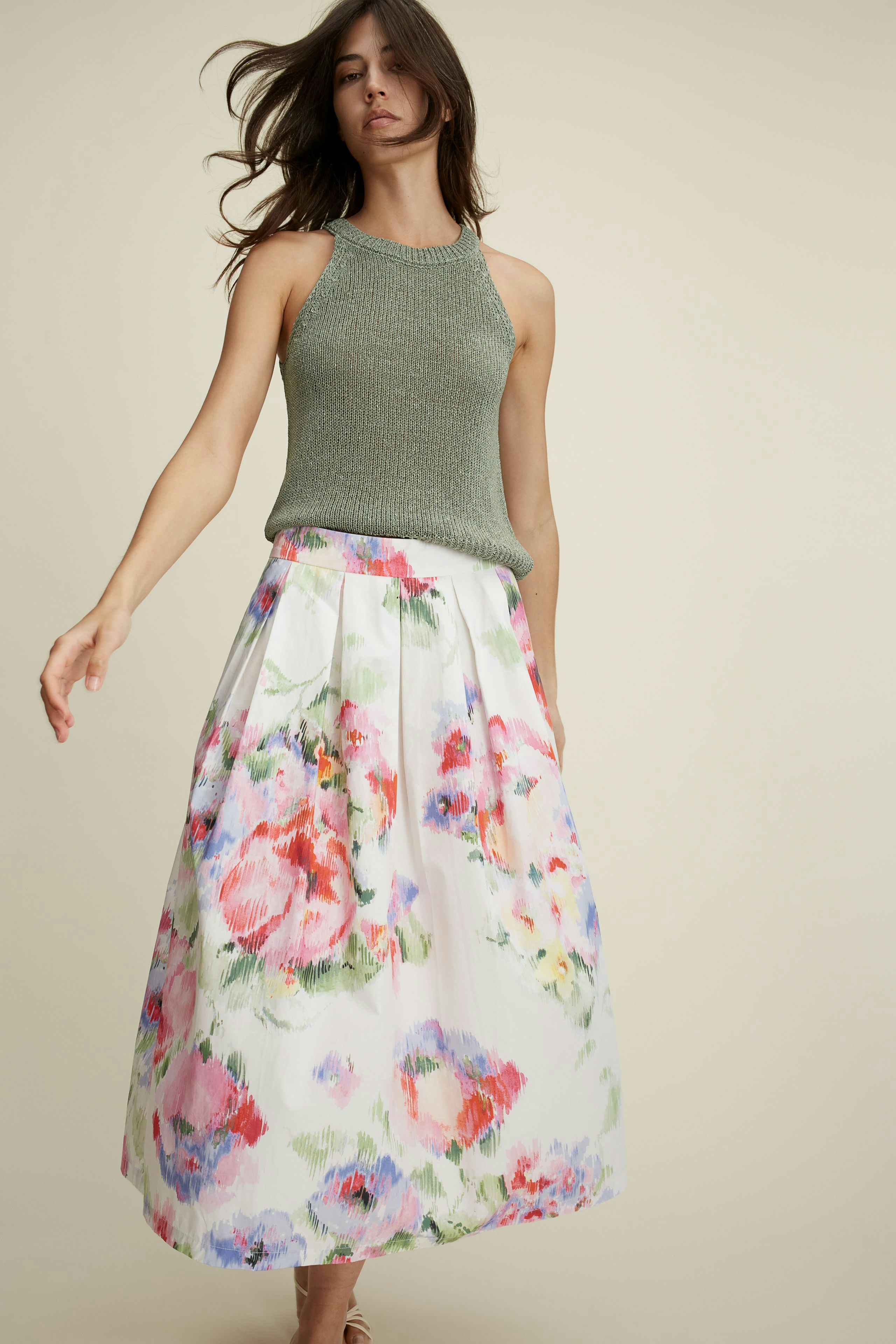 Elegantes Damen-Top: Frau in grauem, ärmellosem Top mit floralem Rock, ideal für den Sommer.