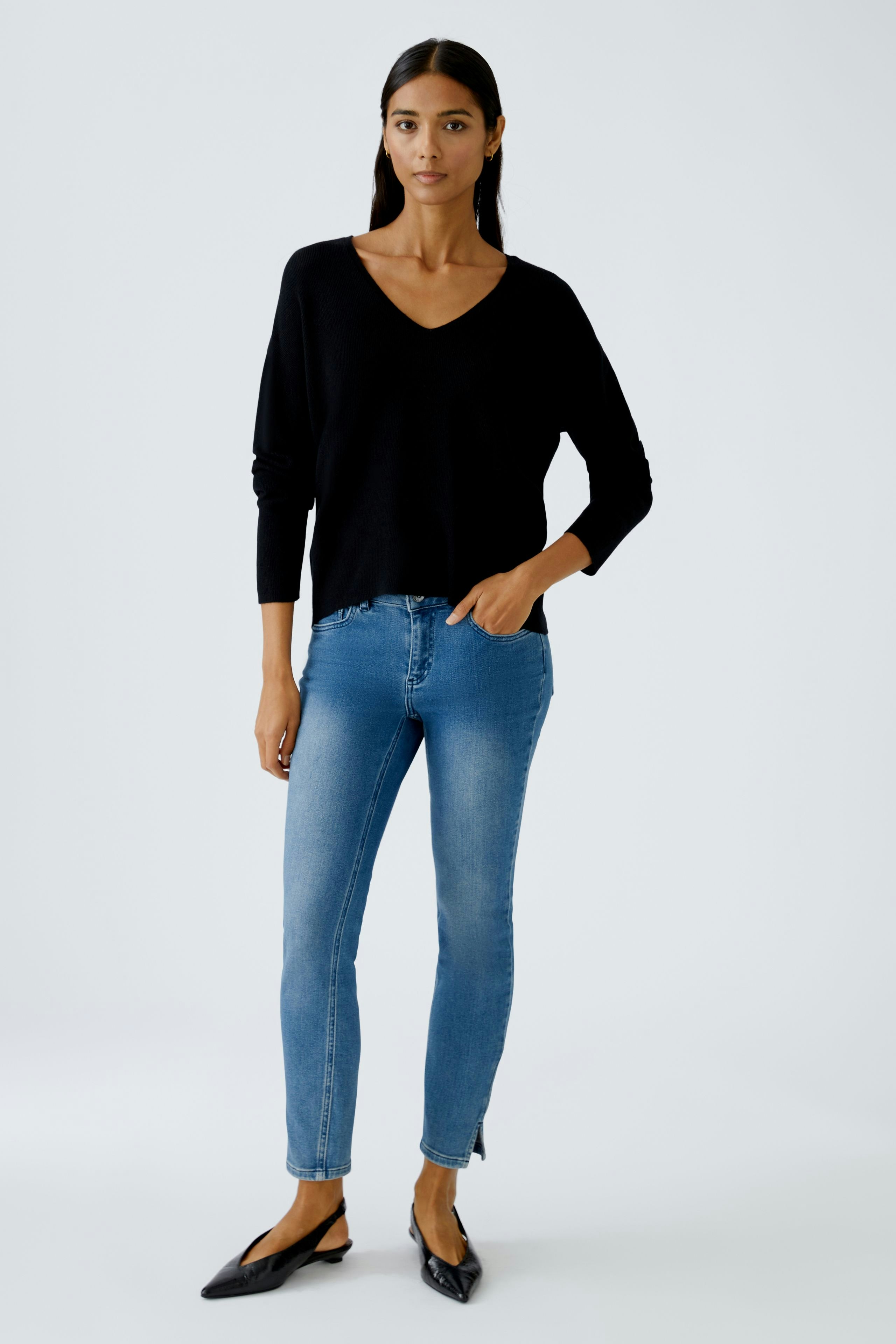 Casual women's pullover: Young woman in a black V-neck pullover paired with blue jeans.
