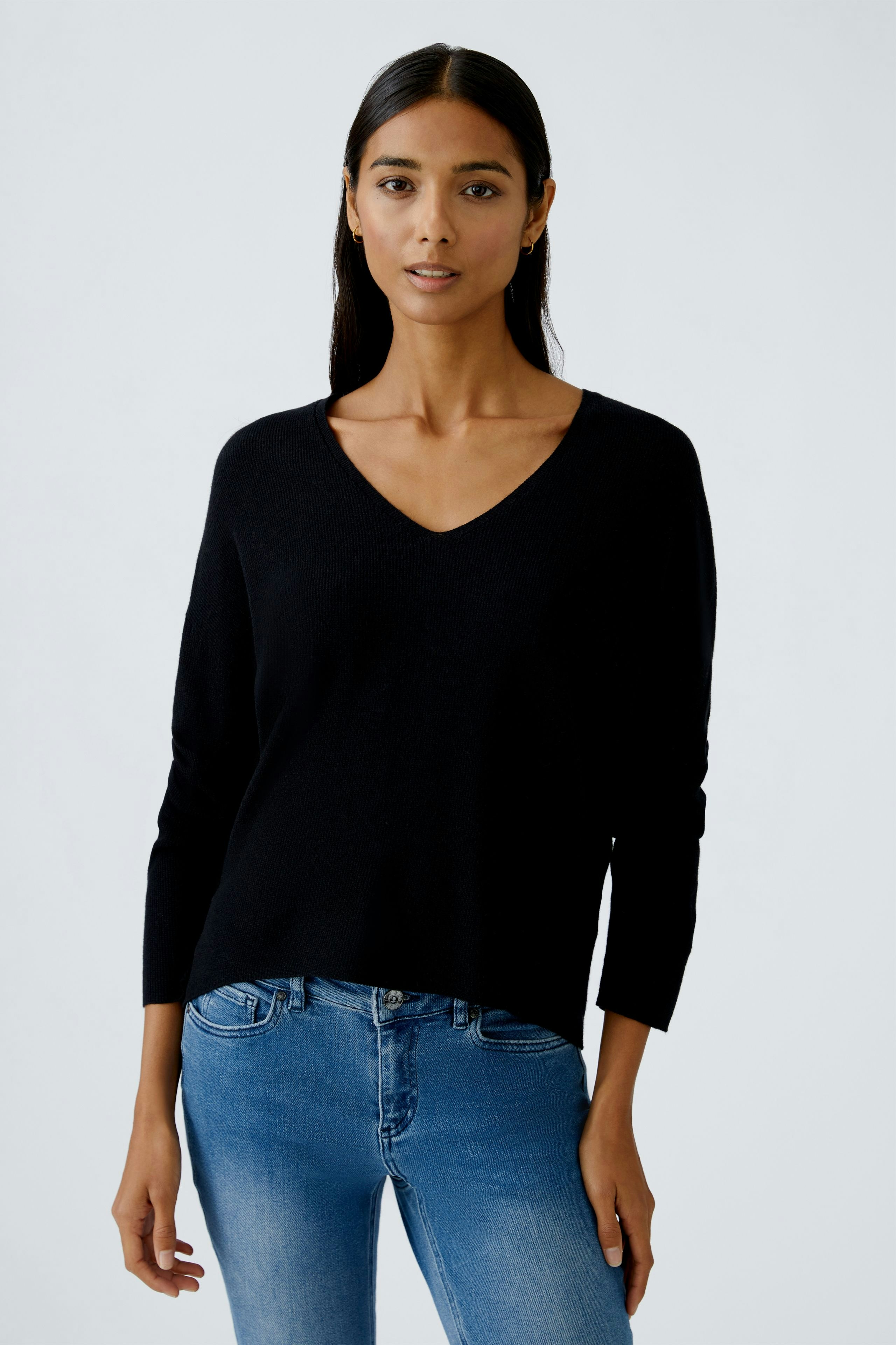Casual women's pullover: Young woman in a black V-neck pullover paired with blue jeans.