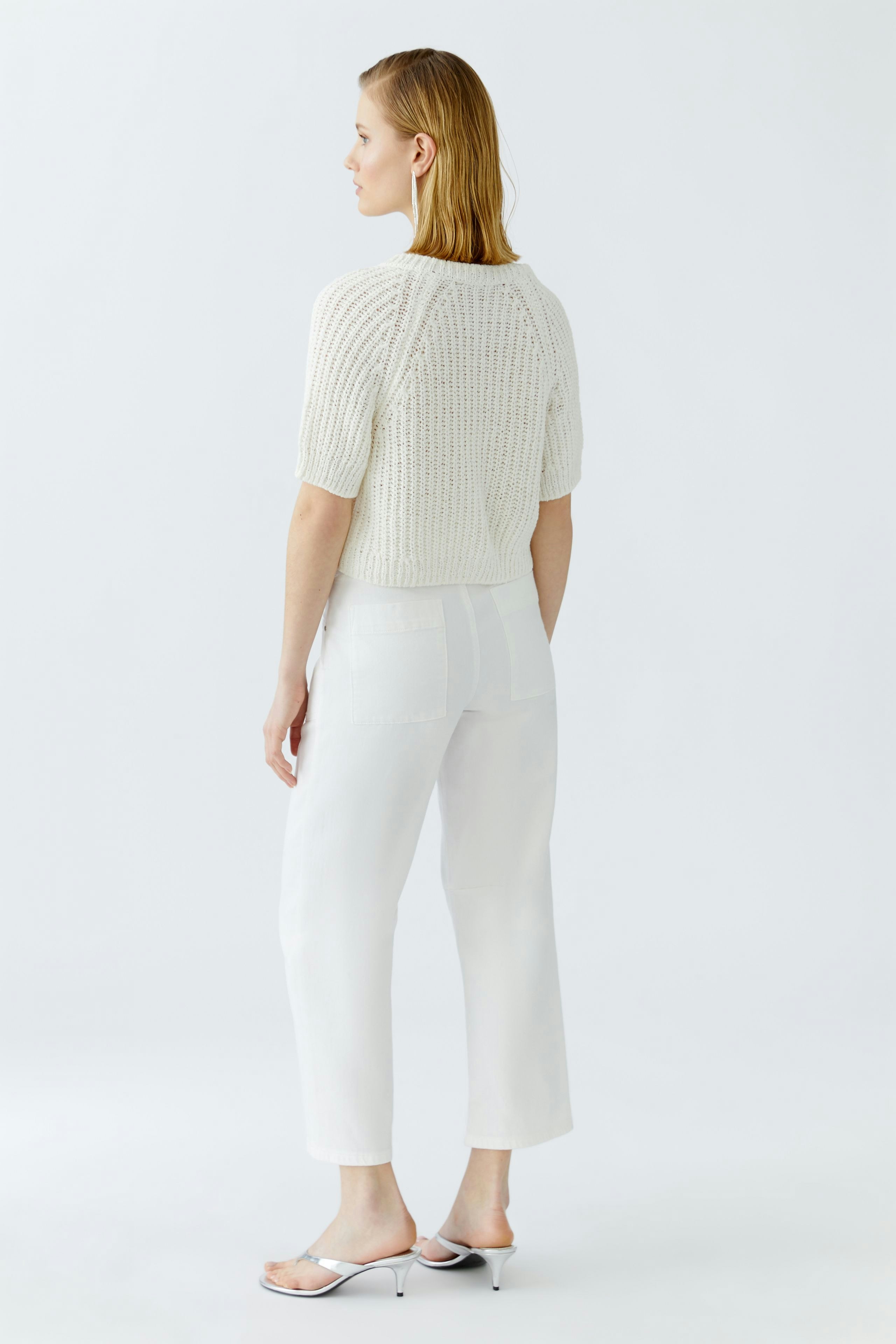 Casual women's cardigan: A woman in a short-sleeved, knitted white cardigan, paired with white trousers.