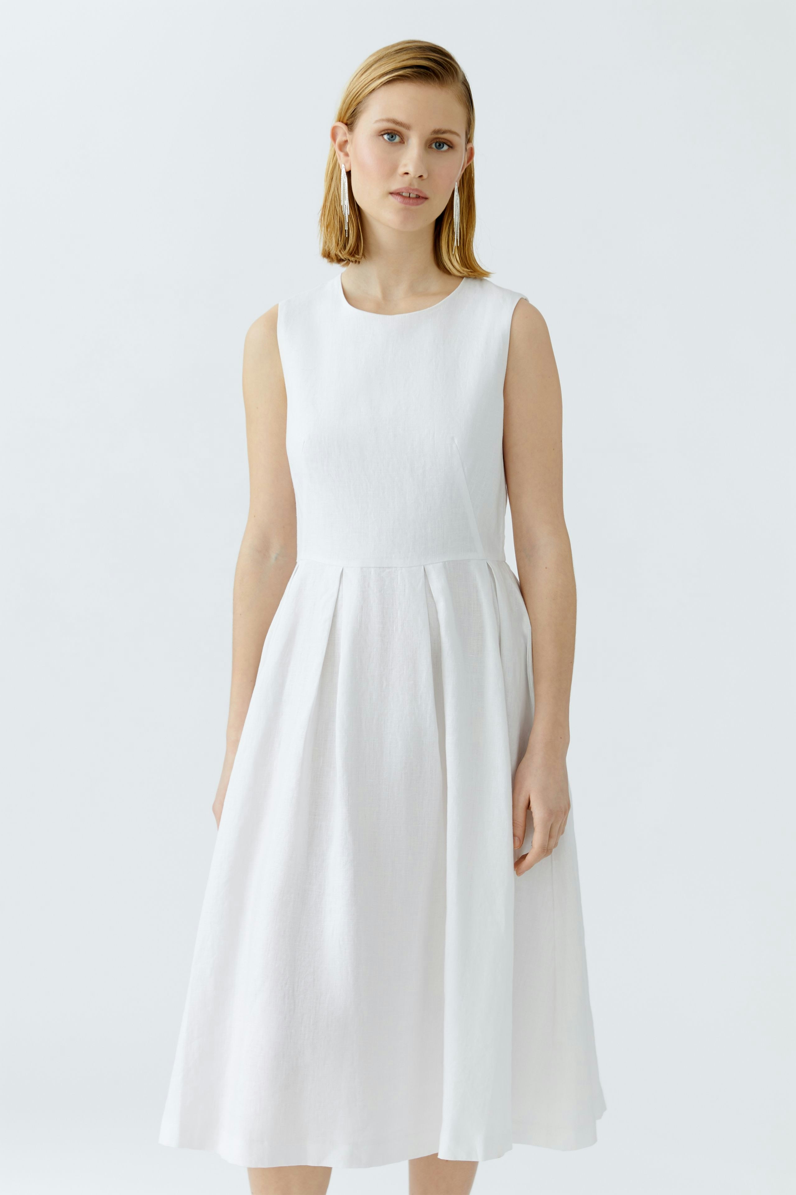 Casual midi dress: Woman in a sleeveless white dress with a flowing skirt, standing confidently.