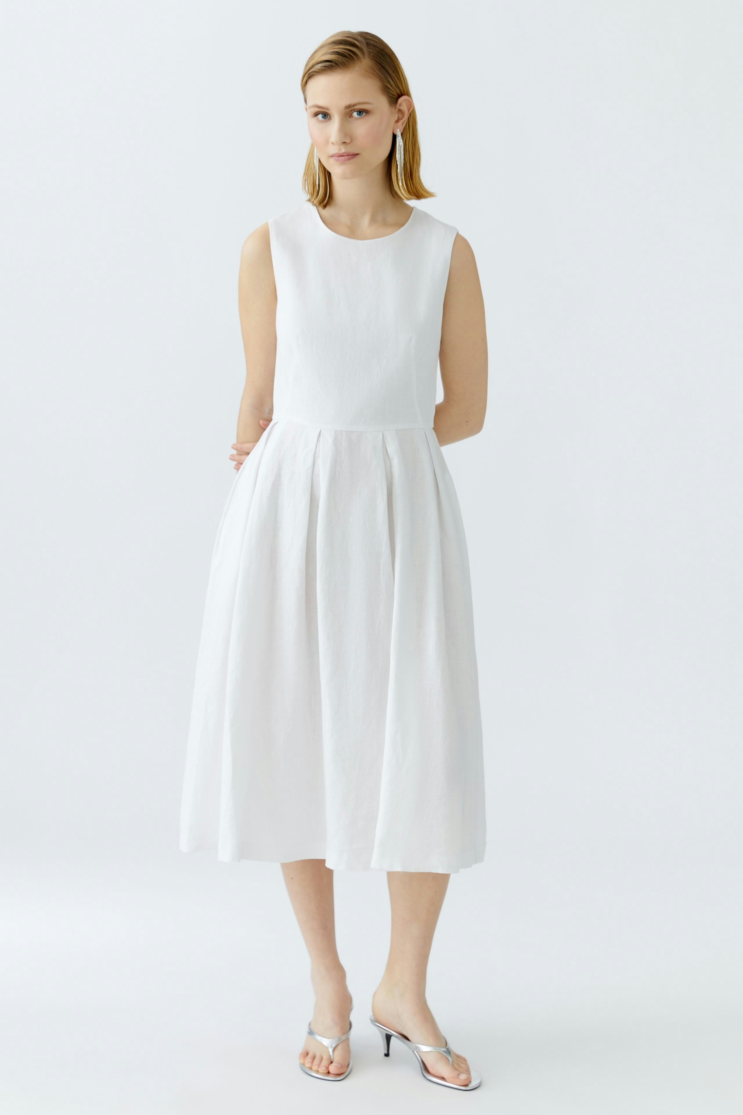 Casual midi dress: Woman in a white sleeveless dress with a flowing skirt, standing confidently.
