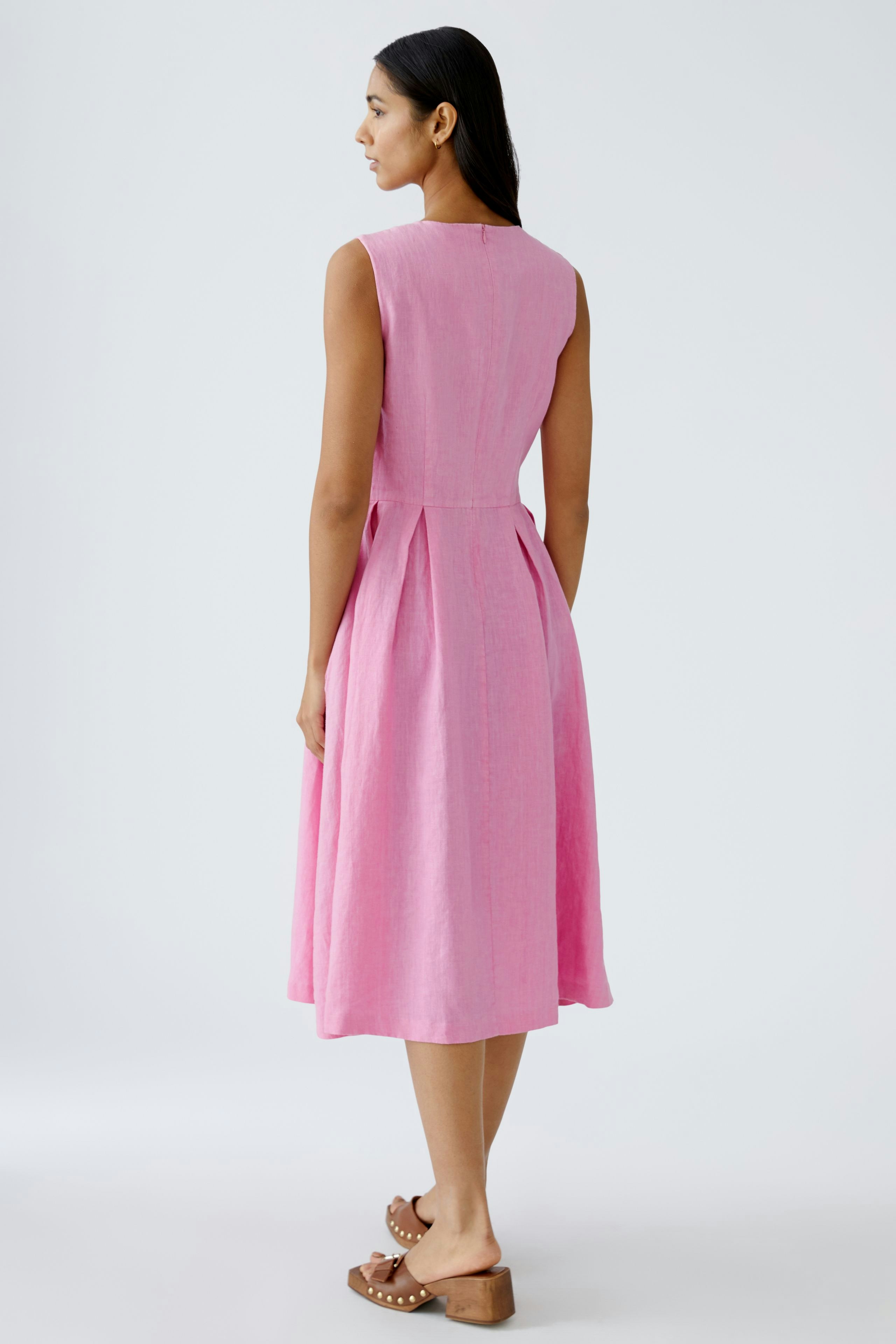 Elegantes Midikleid: Frau in einem pinken, ärmellosen Kleid mit fließendem Schnitt und taillierter Taille.