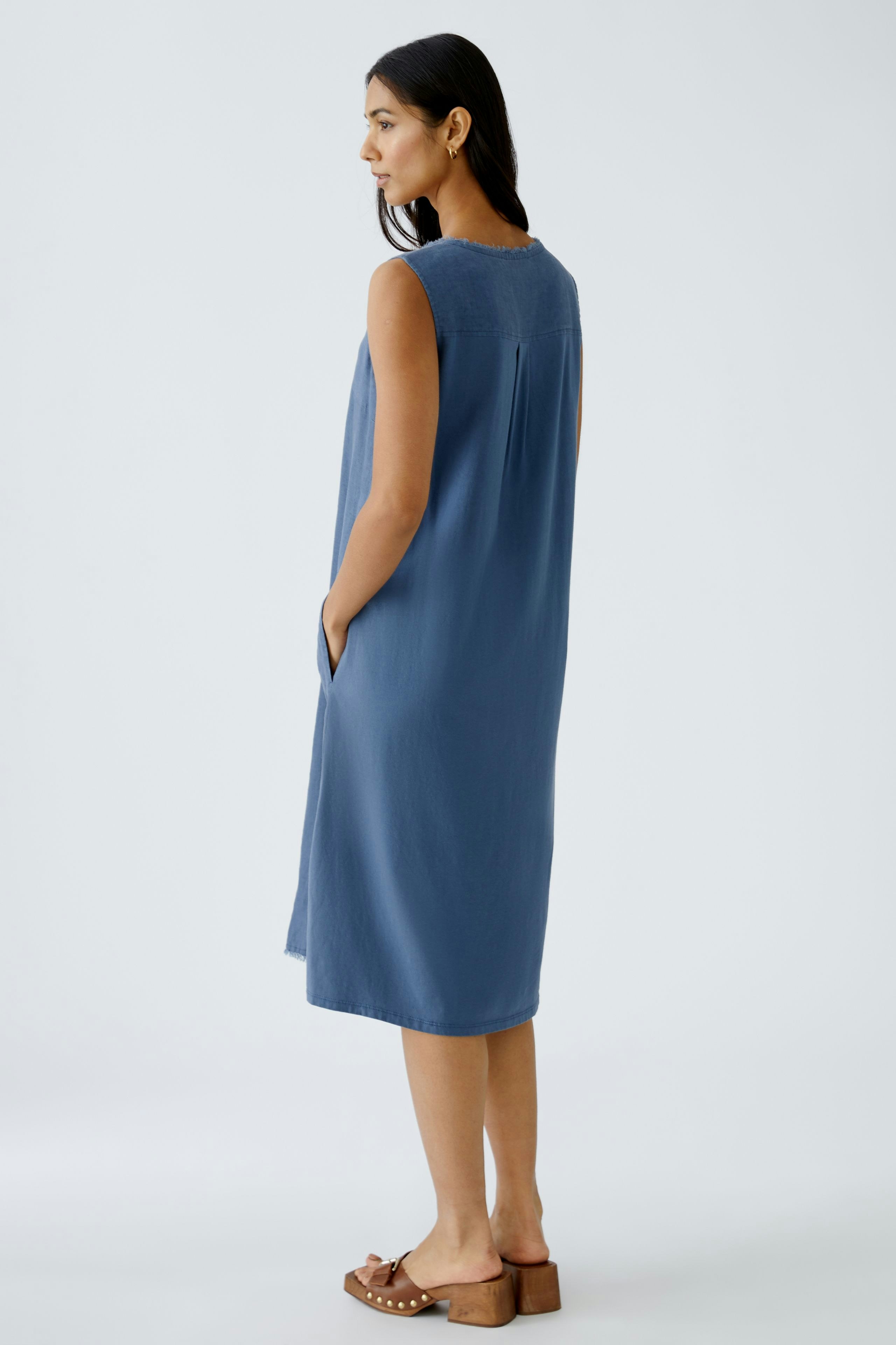 Elegant A-line dress: Woman in a sleeveless blue dress with pockets, showcasing a relaxed silhouette.