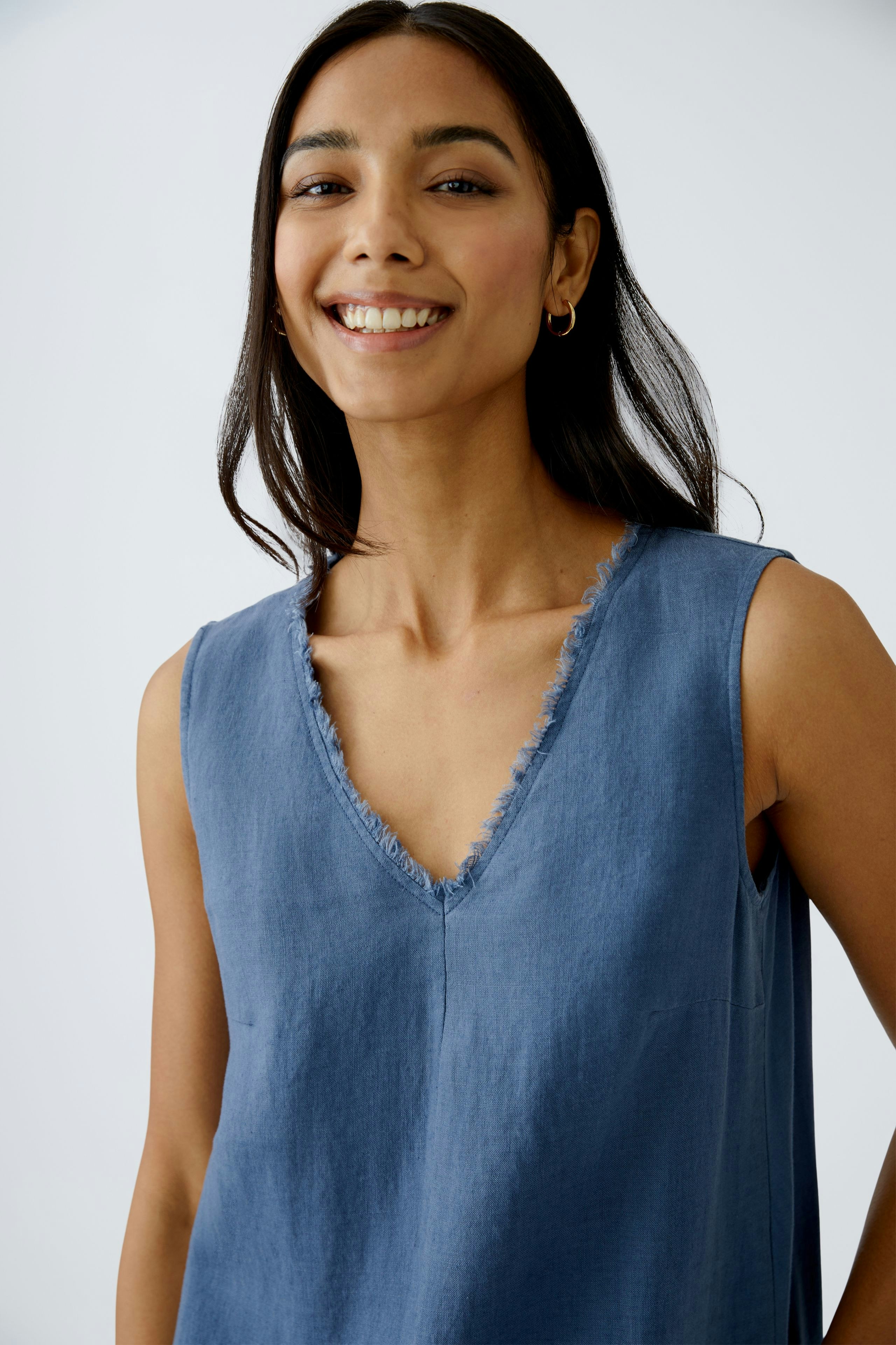A-line dress: A woman smiles in a blue sleeveless dress with a V-neck and frayed edges.