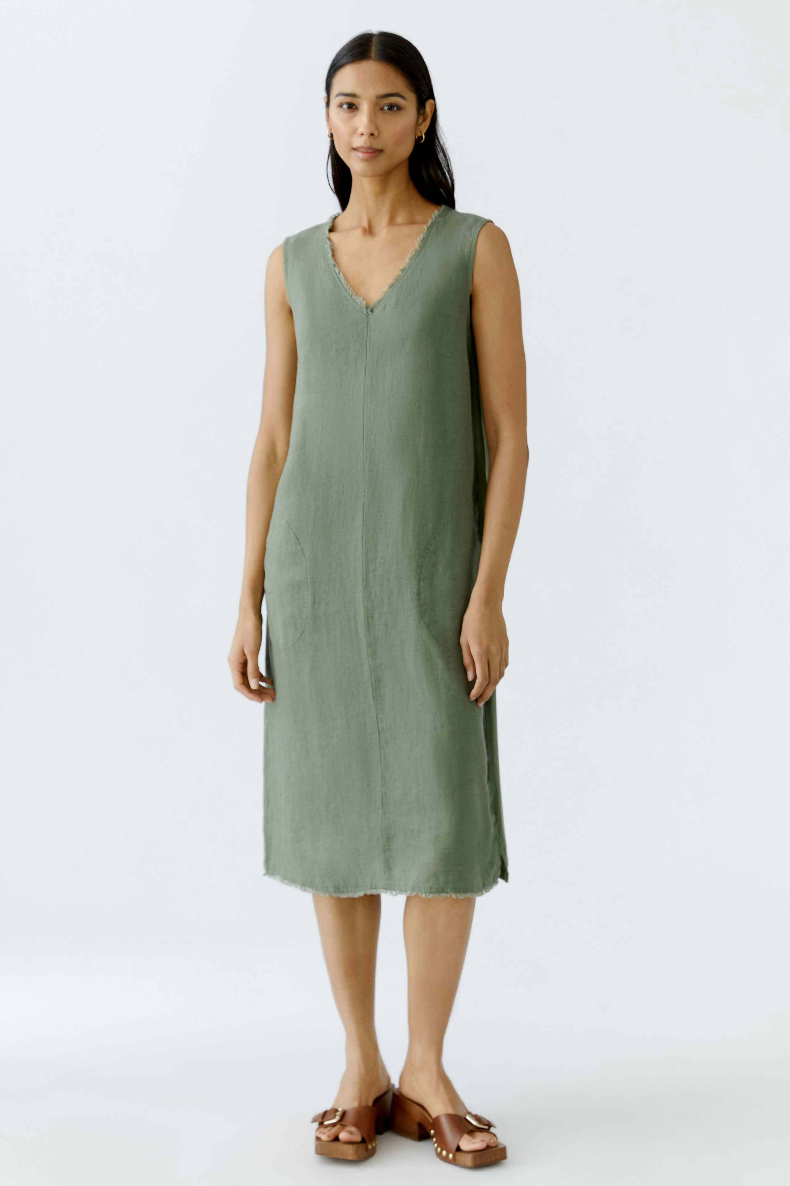 Elegant A-line dress: A woman in a sleeveless, green dress with a V-neckline stands confidently.
