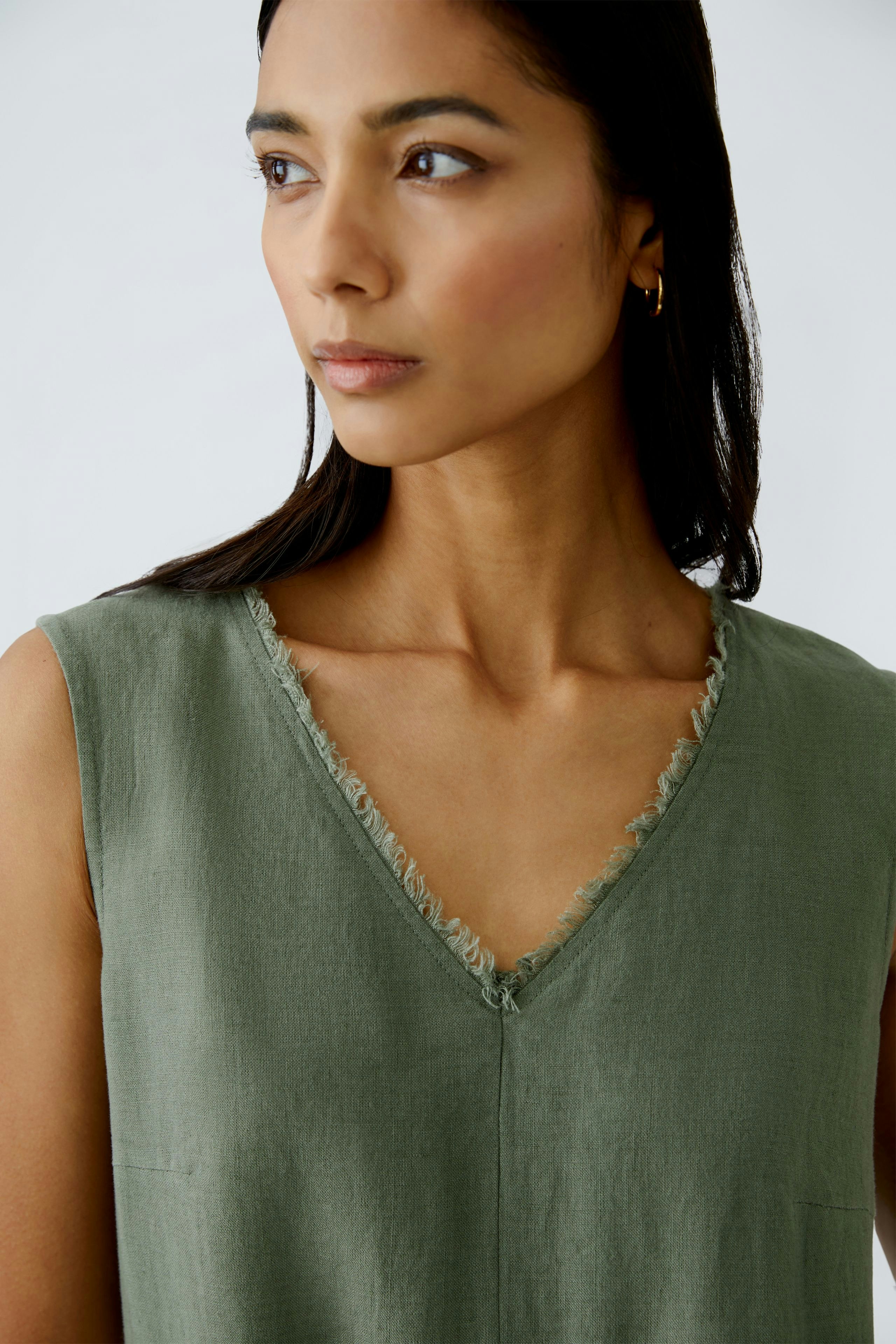 Elegant A-line dress: A woman in a soft green dress with a V-neck and frayed edges, exuding effortless style.