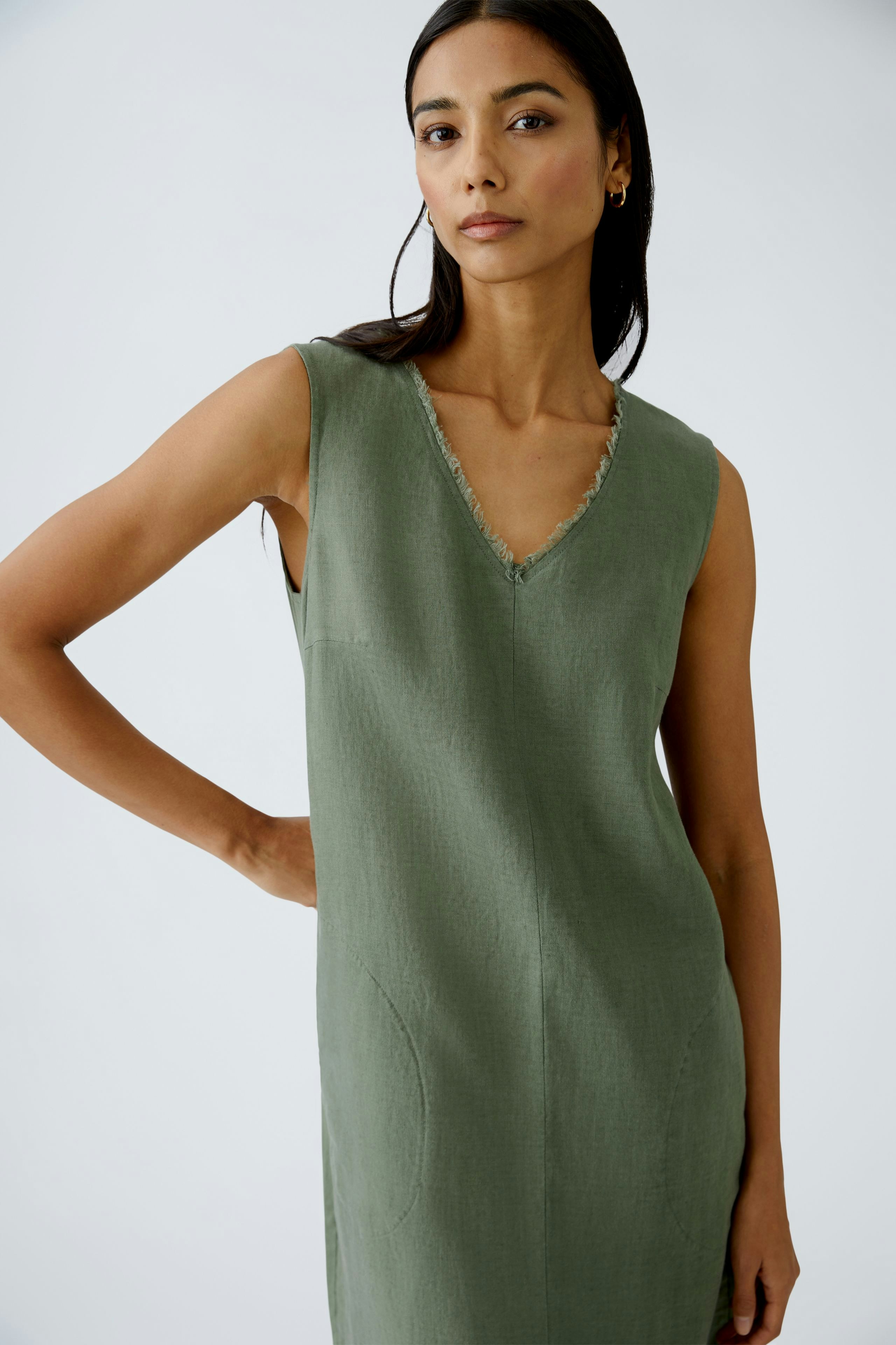 Elegant A-line dress: Woman in a sleeveless green dress with a V-neck, showcasing a minimalist style.